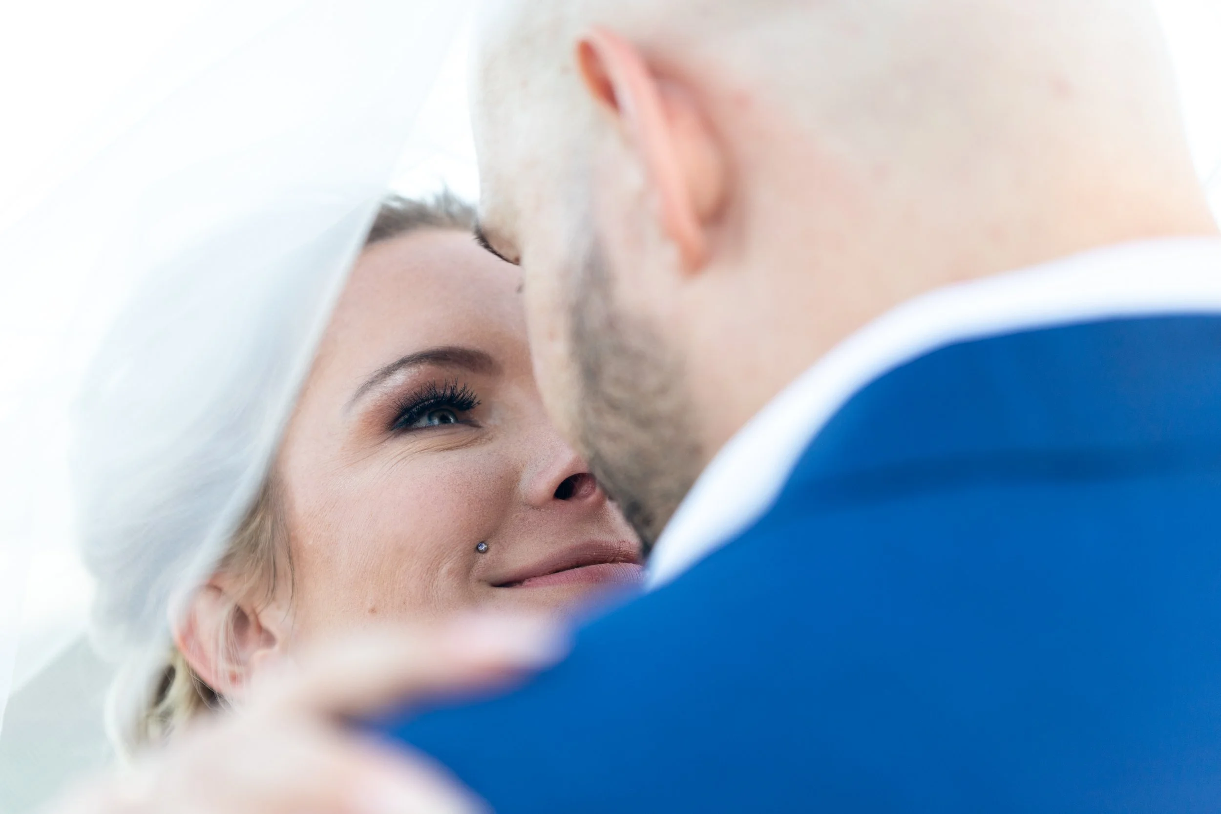 A bride and groom gaze into each other's eyes, with the bride smiling softly and the groom's face partially visible.