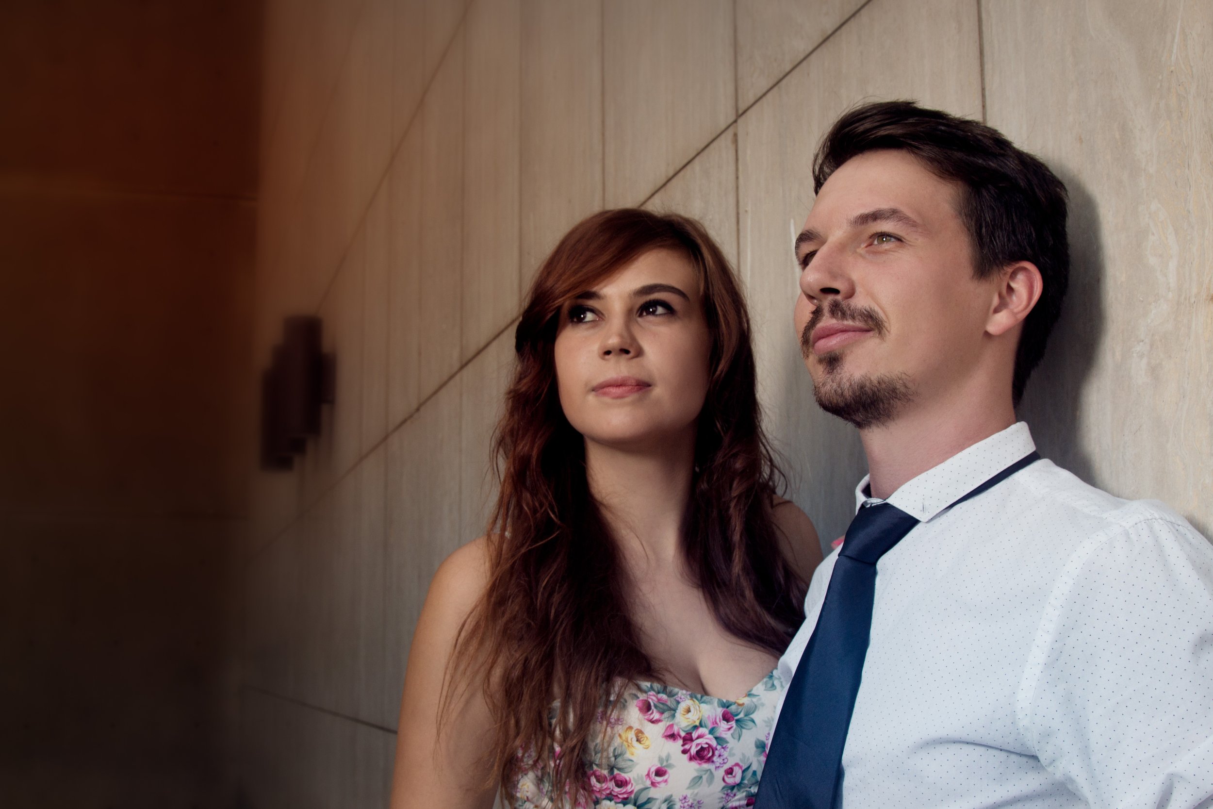 A man and a woman leaning against a wall, looking thoughtfully into the distance.