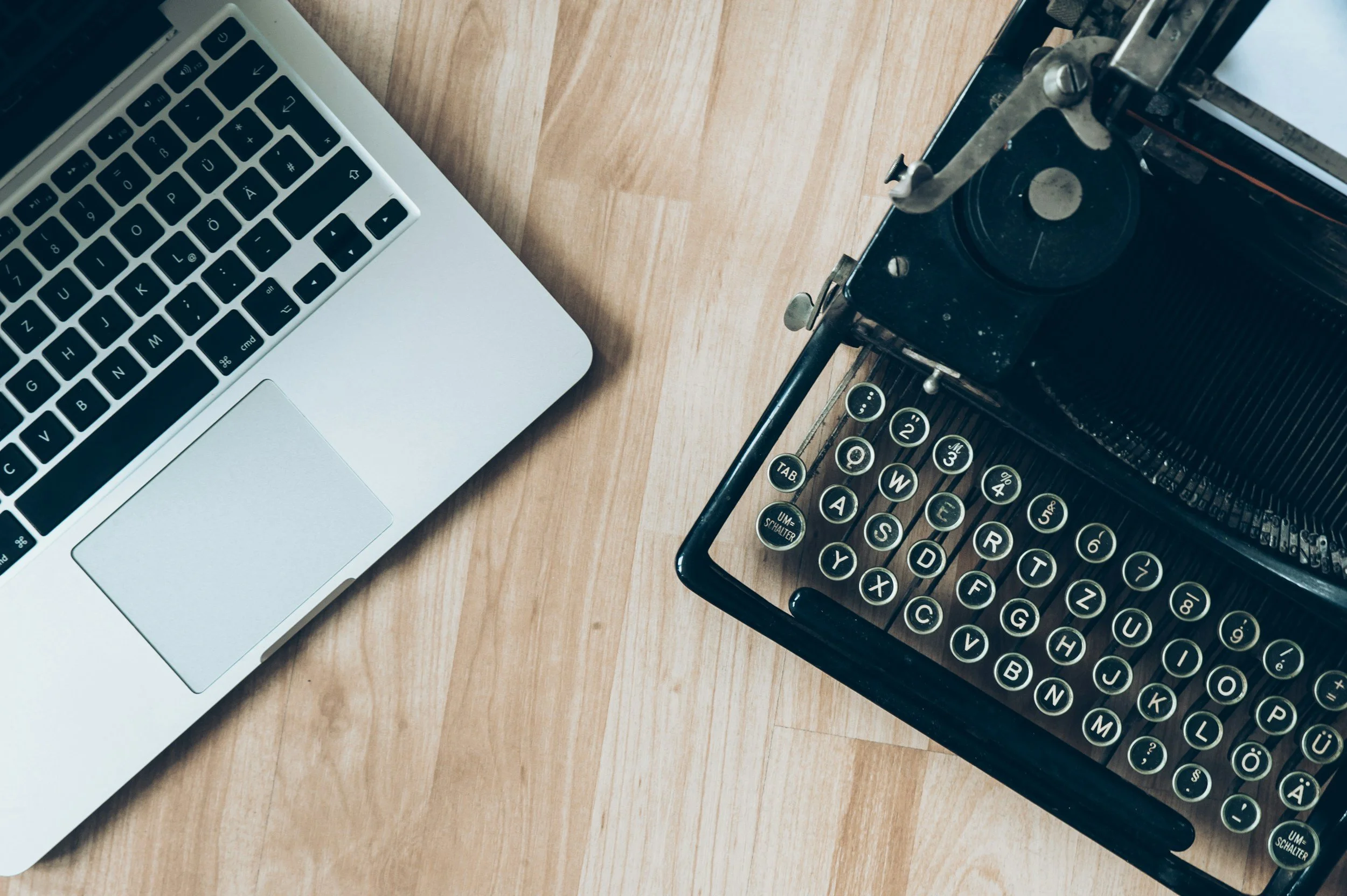 A vintage black typewriter and a silver laptop on a wooden desk.