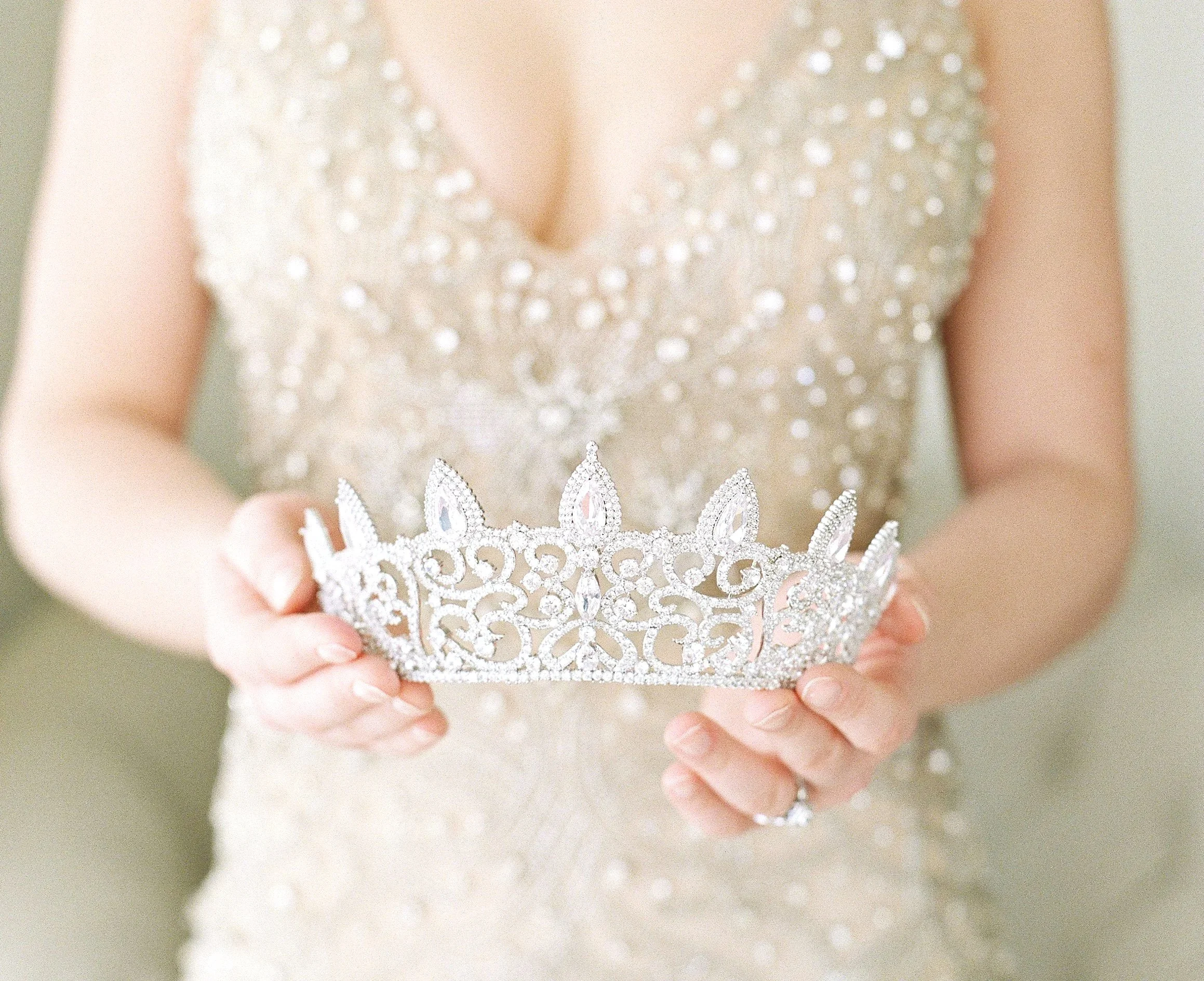 A young beautiful busty blonde or brunette cutie in a sparkly, embellished dress holding a luxurious platinum or white gold tiara with diamonds.