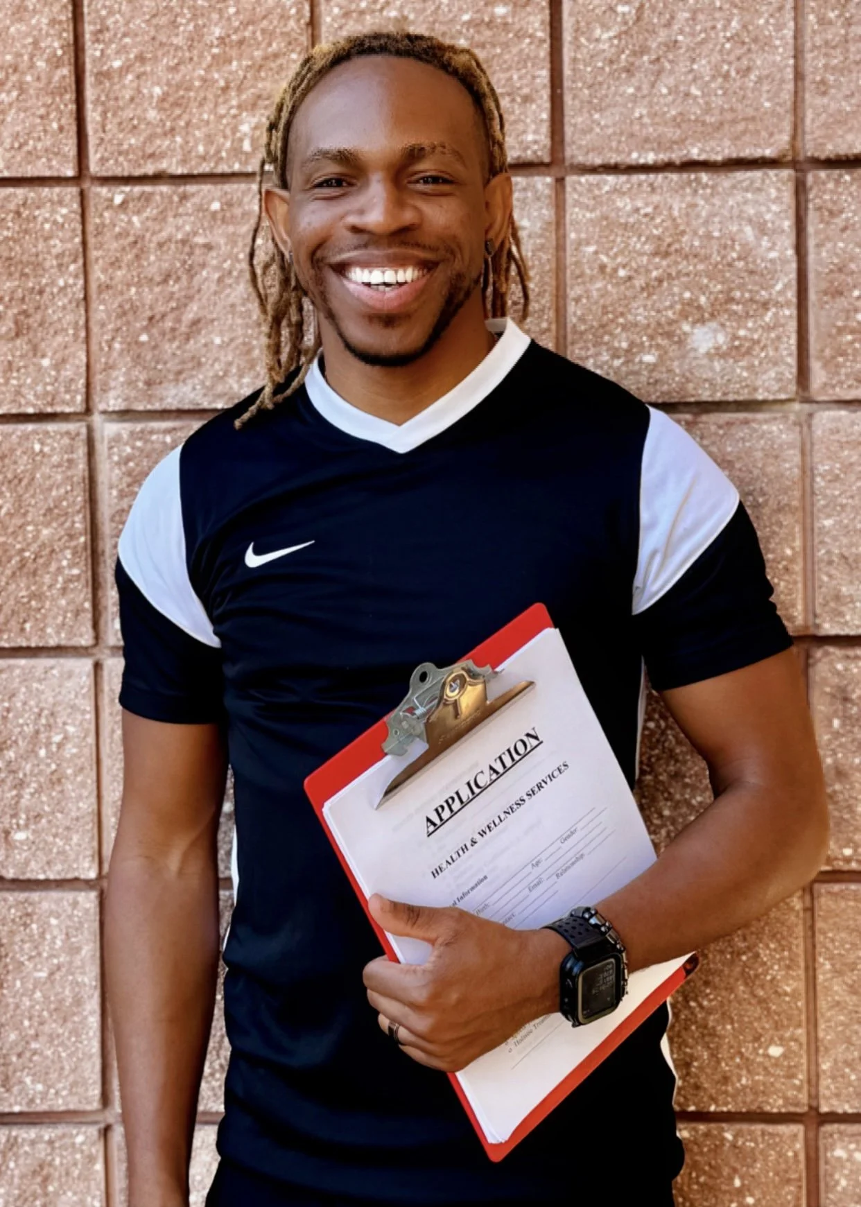 Coach Howard handsome, successful, athletic, fit black man smiling while holding an application for health and wellness services, standing against a brick wall.