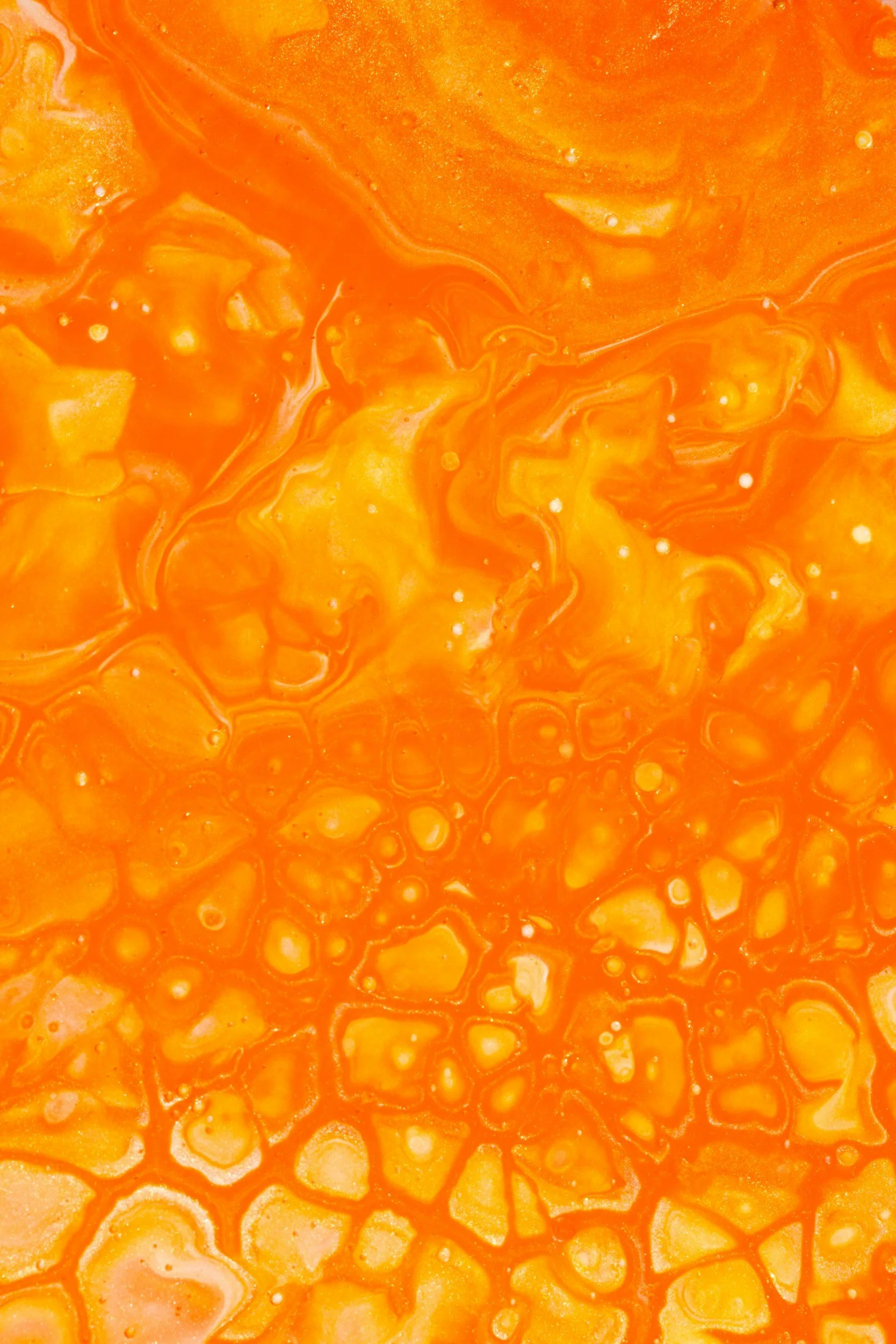 Close-up of a brightly colored orange and yellow marbled liquid with swirling patterns and small bubbles.