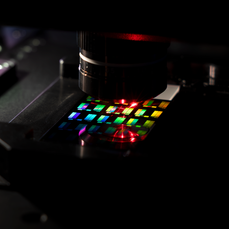 Microscope examining a colorful nanophotonic wafer with a red laser light.