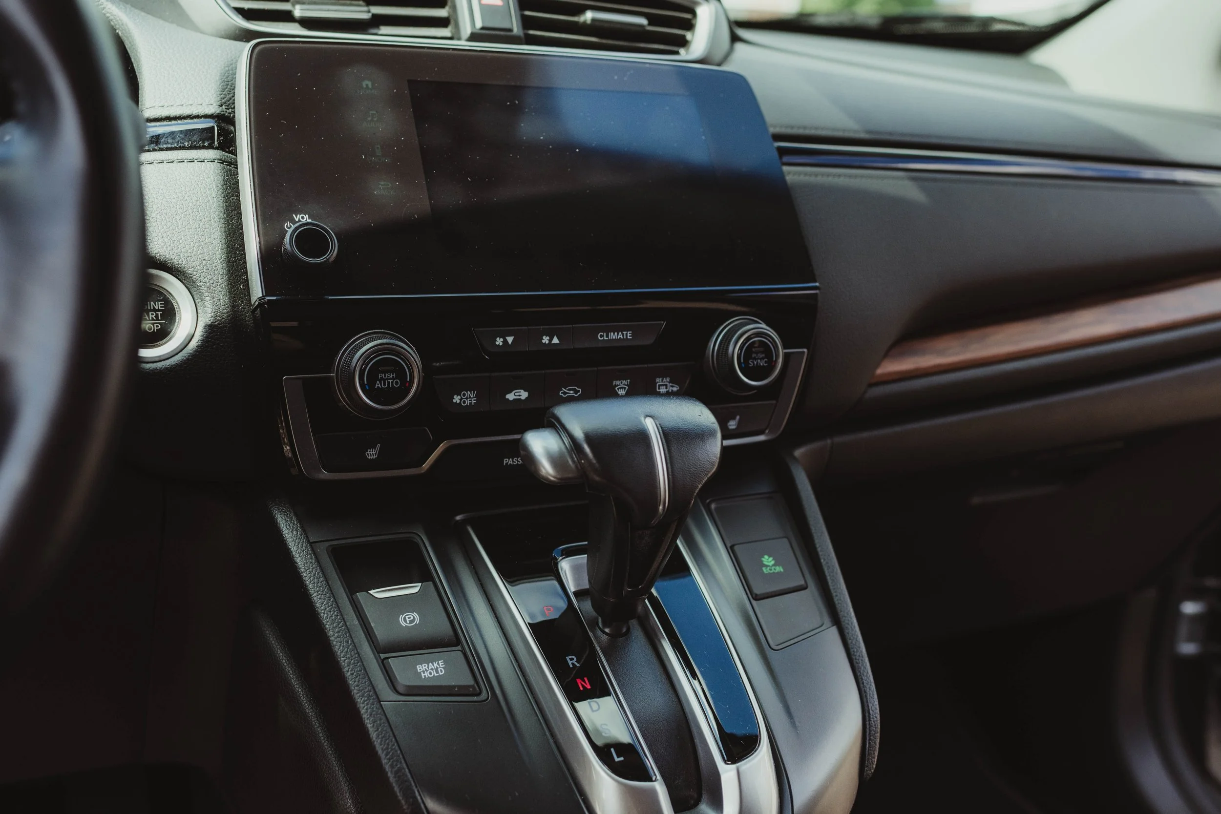 Interior of a car showing the gear shift lever and dashboard controls, including a large touchscreen display, climate control buttons, and various driving options.