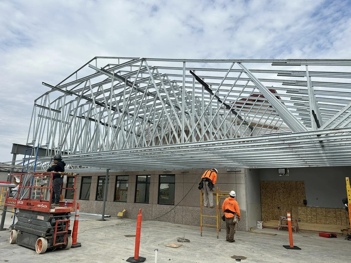 Construction workers installing a metal framework on a building with cloudy sky background.