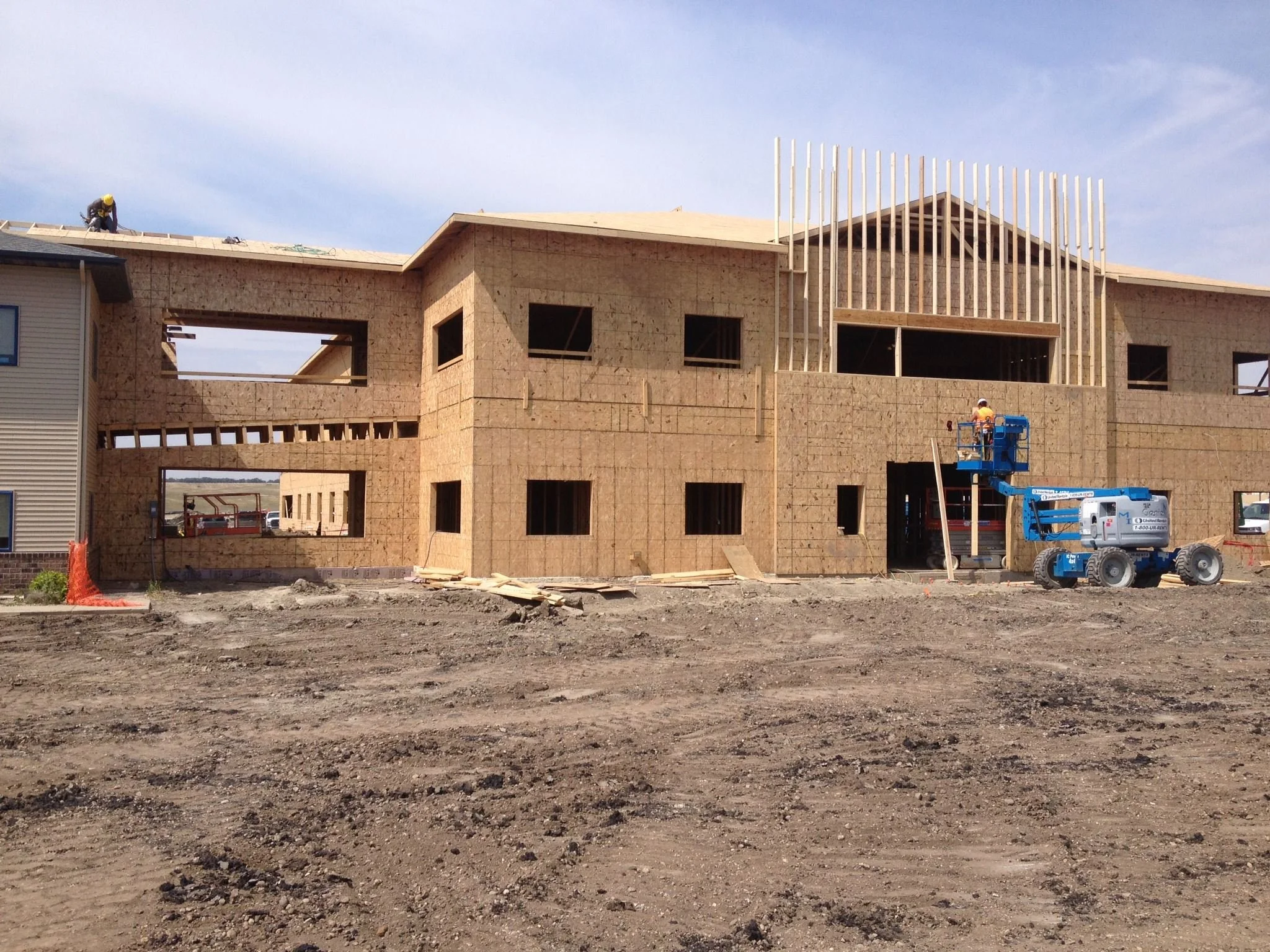 Construction site of a multi-story building with partially installed framing and workers using a blue lift.