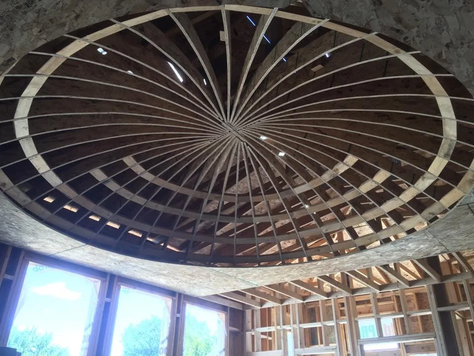 Interior view of a circular wooden ceiling structure with radial beams, in a house under construction.