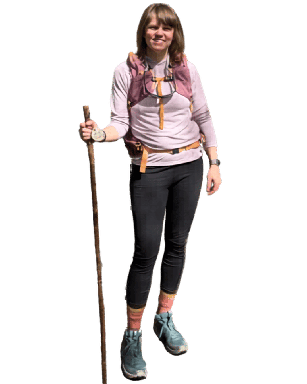 a white woman with medium brown hair wearing hiking gear including a backpack and walking stick smiles at the camera.
