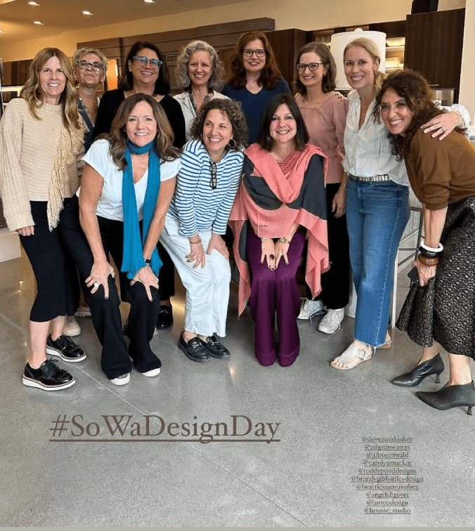 Group of twelve women smiling and posing together indoors. Some are standing, some are crouching or sitting in front. The women are dressed casually, and the setting appears to be a modern interior. The hashtag #SoWaDesignDay is visible at the bottom of the image.