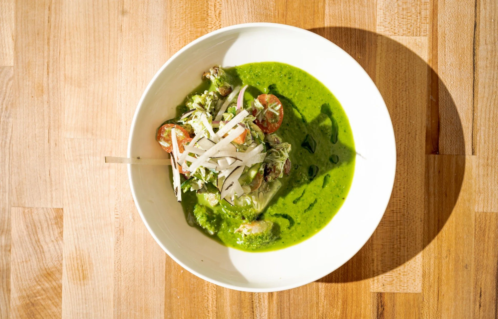 A bowl of green soup with chopped vegetables on top, placed on a wooden surface.