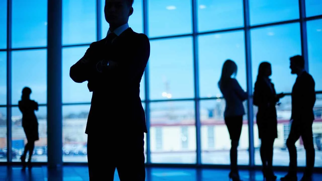 Man standing separately from other people in a glass building