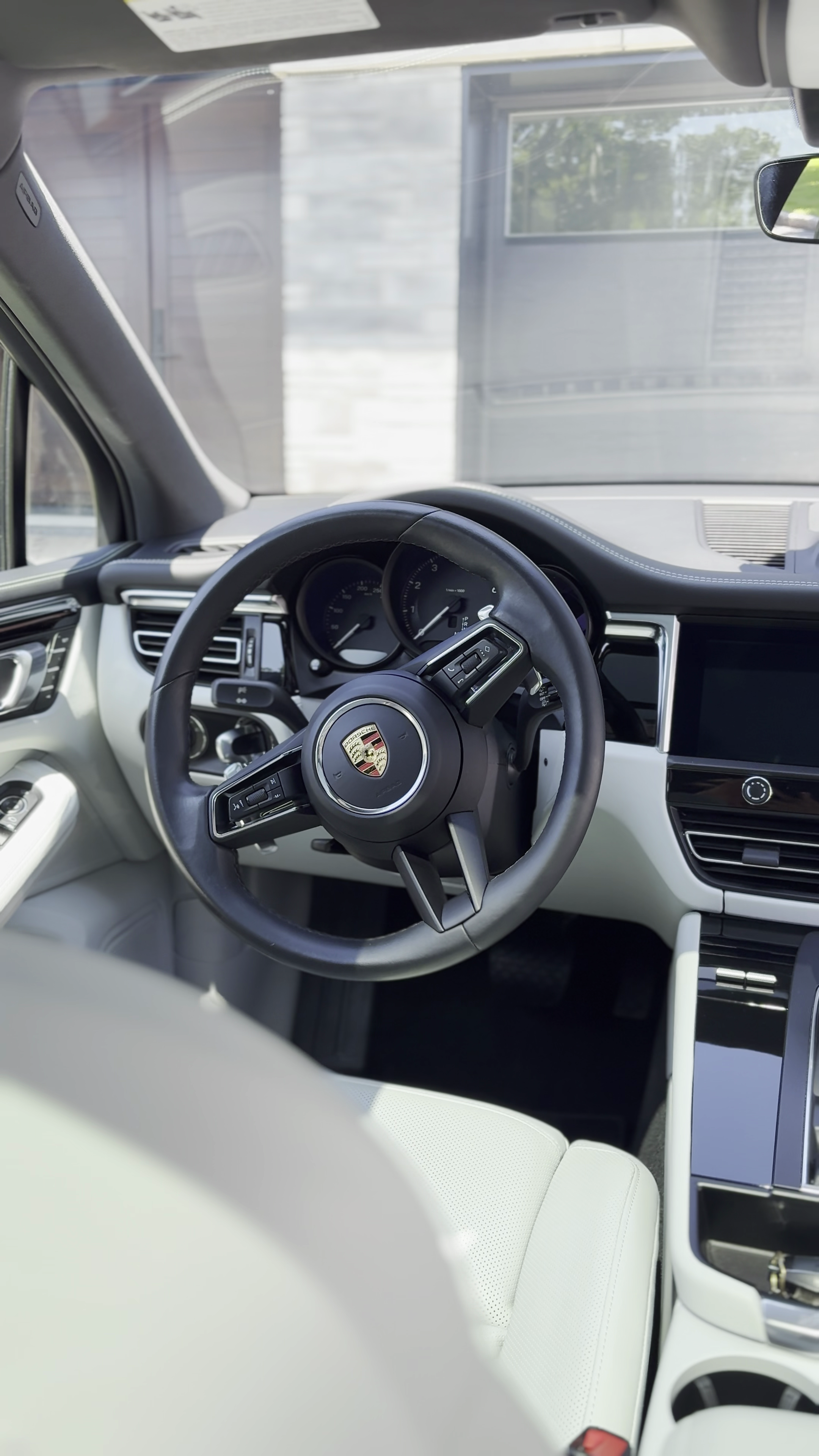 Intérieur d'une voiture Porsche avec volant, tableau de bord et écran central, vue depuis le siège conducteur.