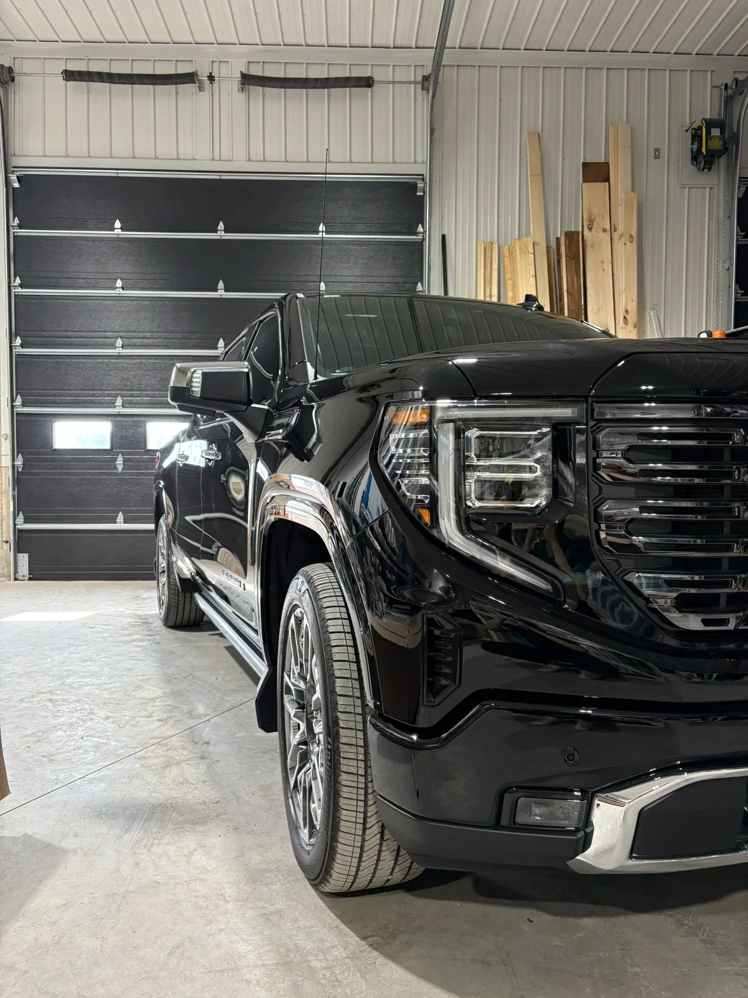Voiture noire dans un garage avec un mur en tôles et des planches de bois contre le mur.