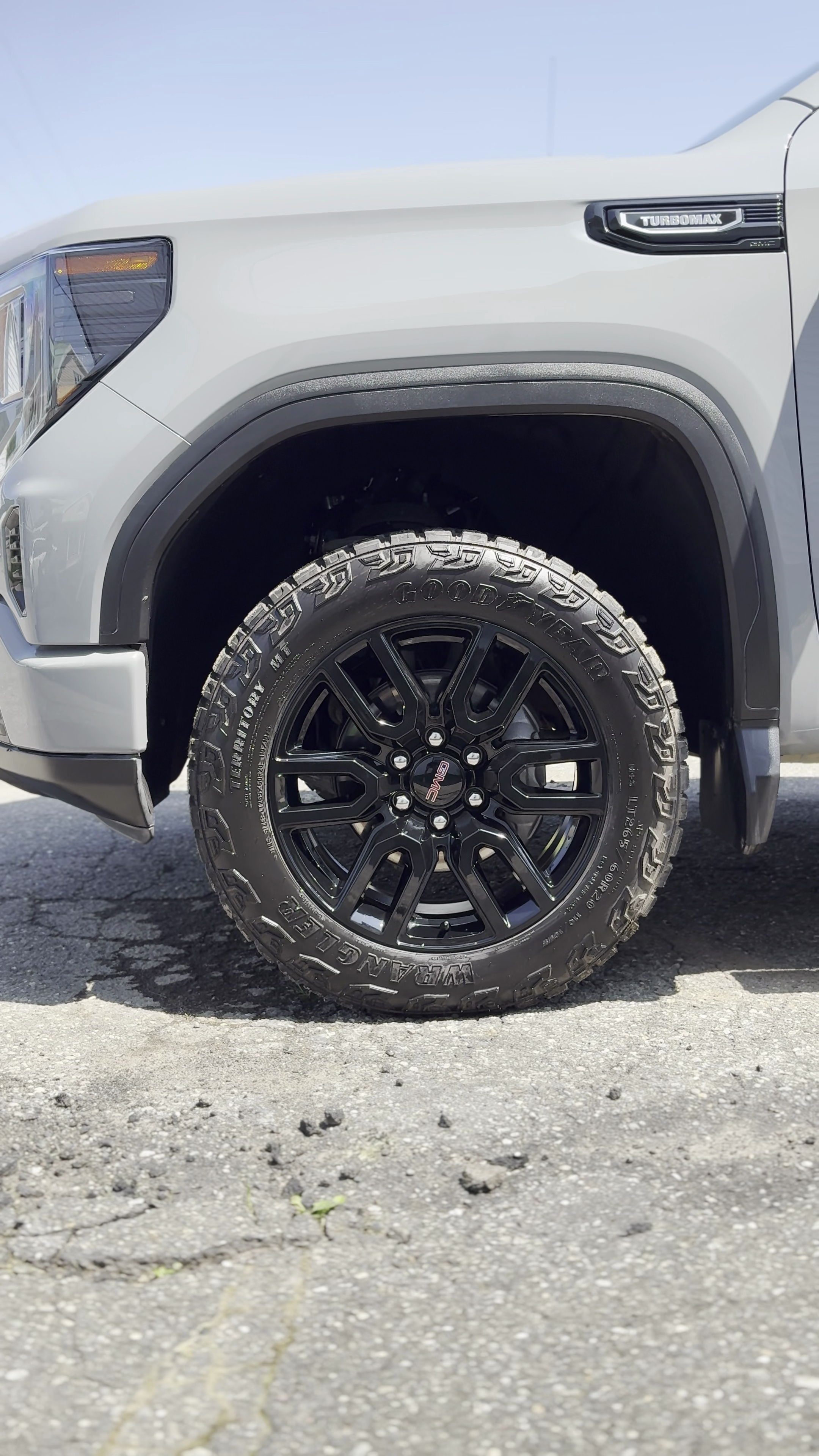 Une roue de véhicule tout-terrain, avec un pneu Goodyear Warrantor, monté sur une jante noire, avec la visibilité partielle du pare-chocs avant d'un véhicule gris.