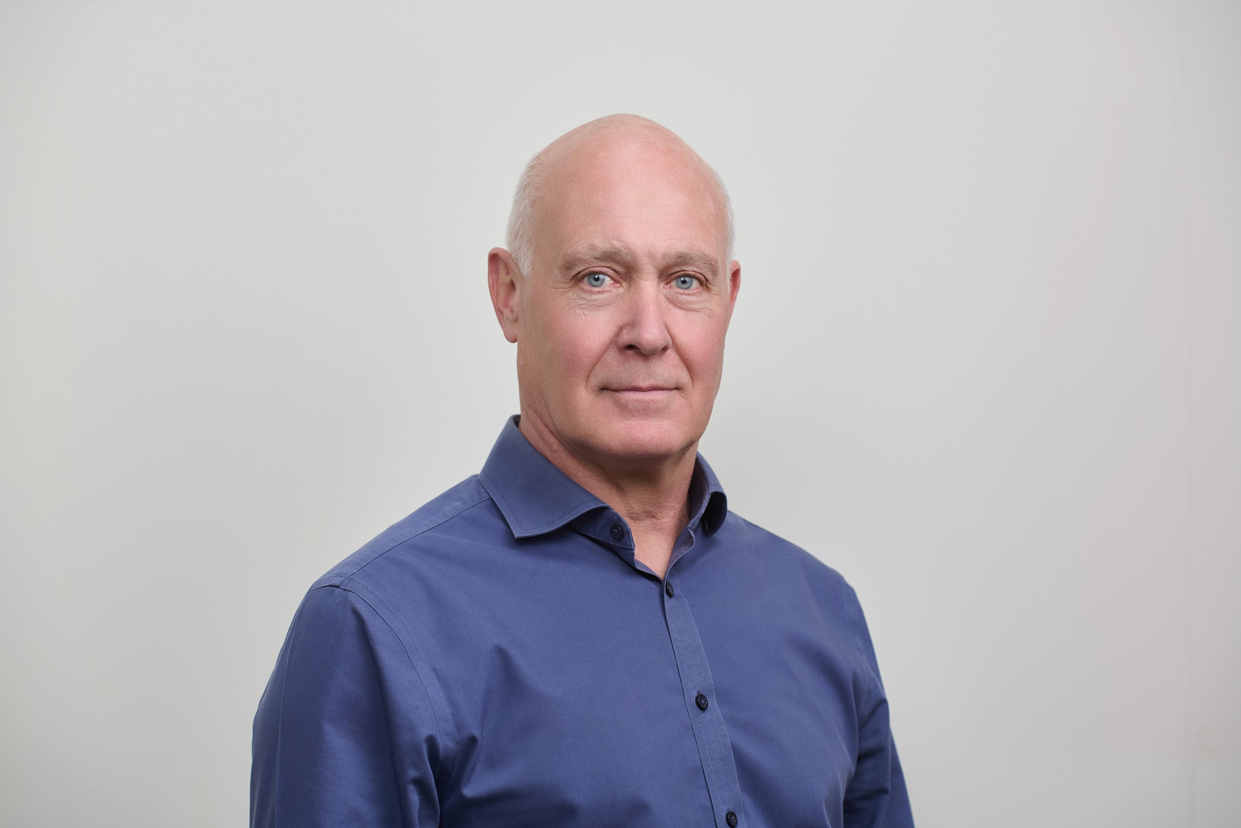 A headshot of Dr William Hopkins wearing a blue button-up shirt, standing against a plain light grey background.