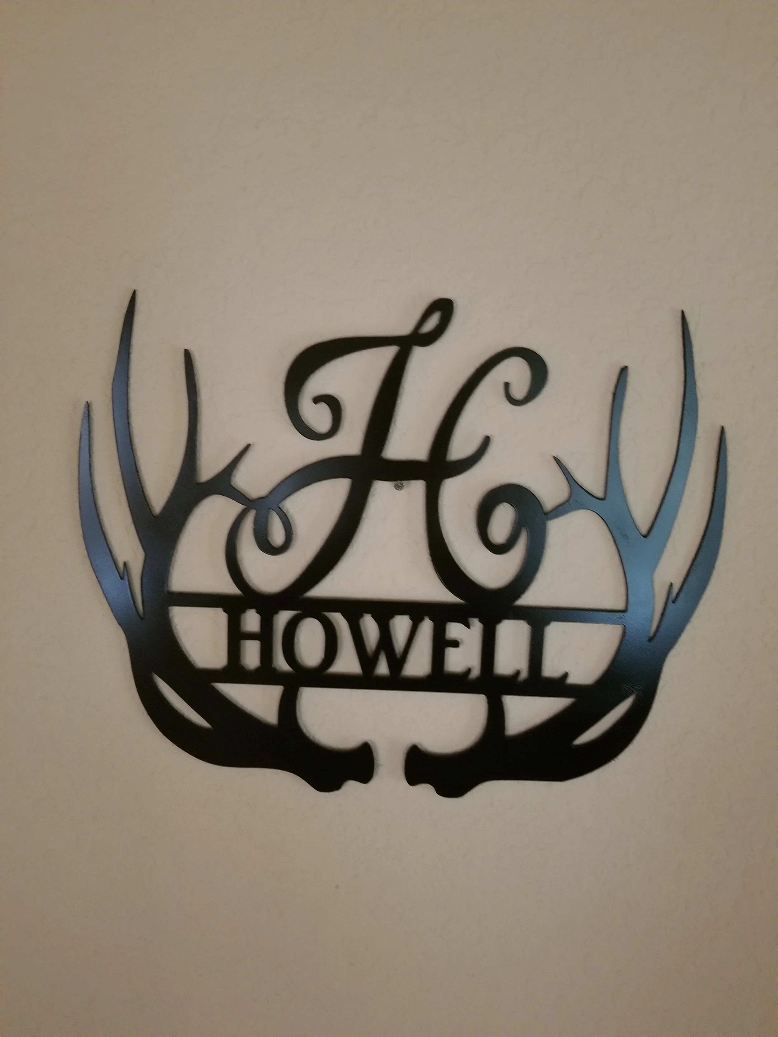 A black decorative sign with the words 'This Is How We Show Love' in cursive, surrounded by a floral design, mounted on a beige wall.