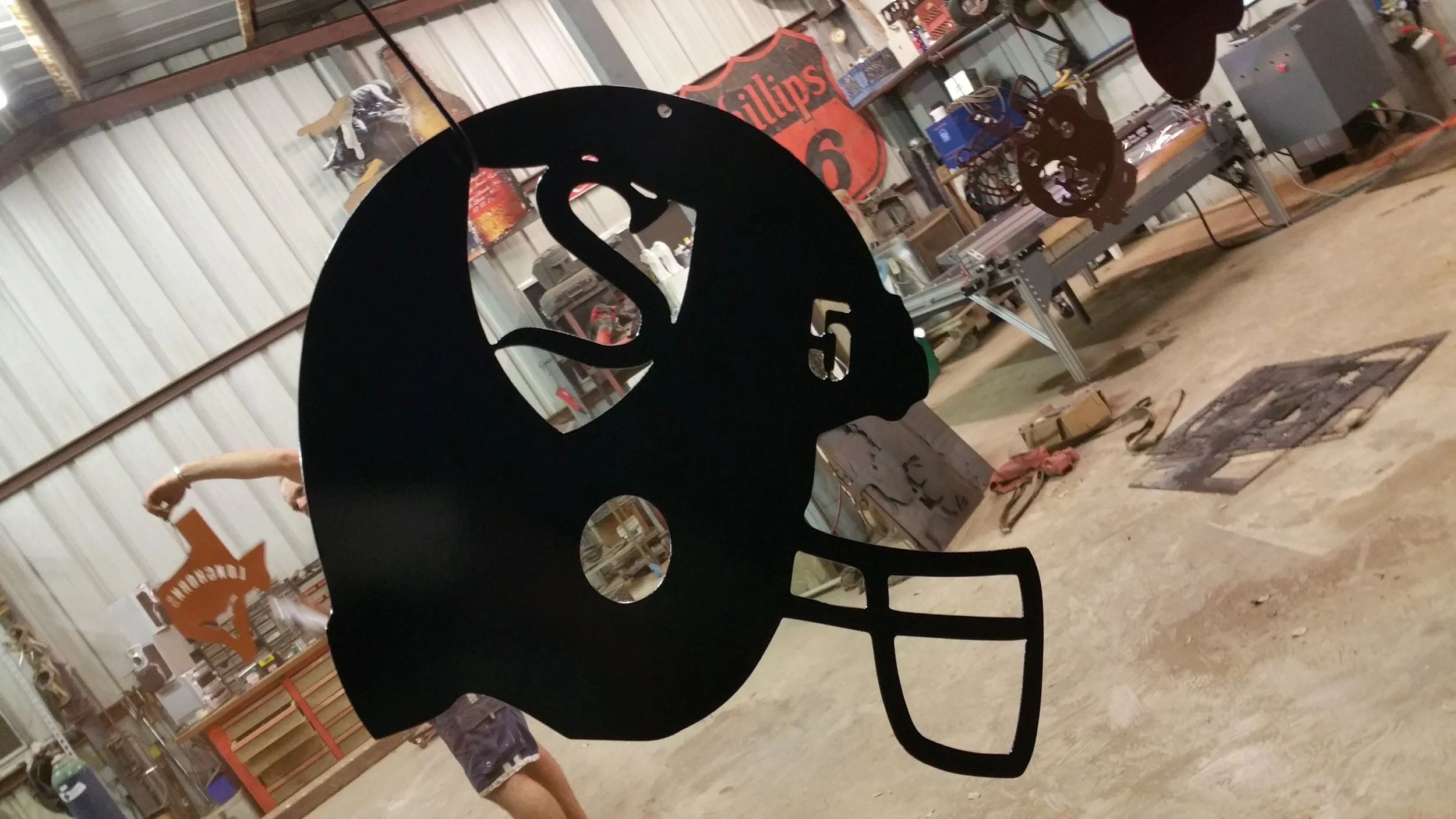 A metal skull-shaped cutout in a workshop with various tools, signs, and equipment in the background.