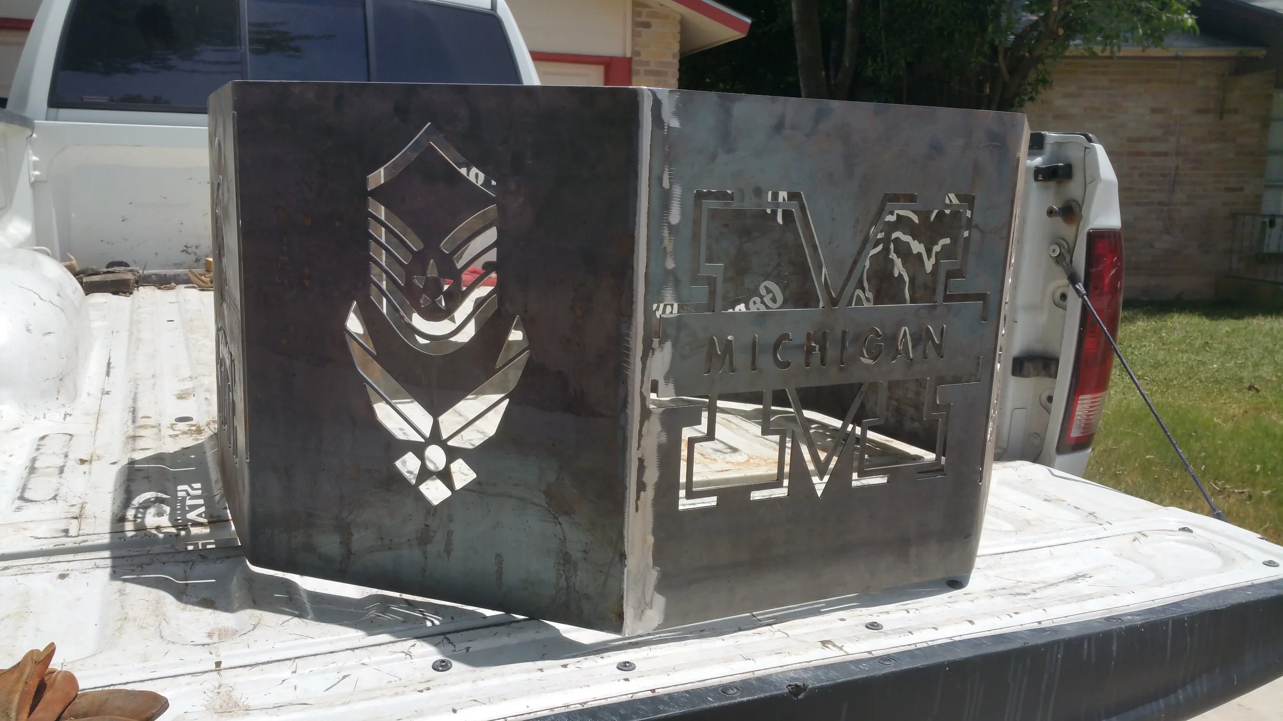 Metalblock with cutout designs including a bee and the word 'LOVE' with 'MICHIGAN' beneath it, placed in the back of a pickup truck.