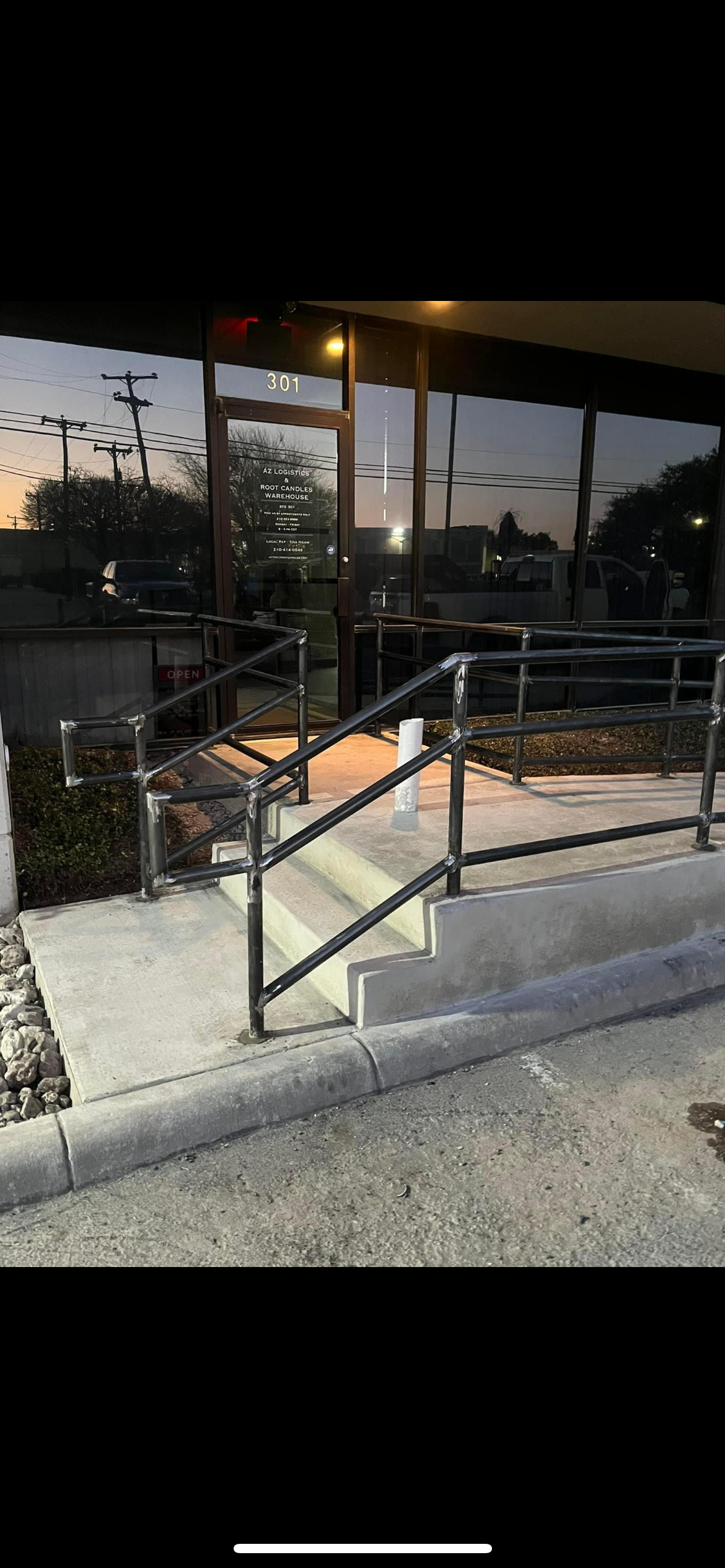 Outside view of a glass storefront building with a ramp and stairs, titled 'AZ Logistics & Root Candles Warehouse' at 301, during dusk