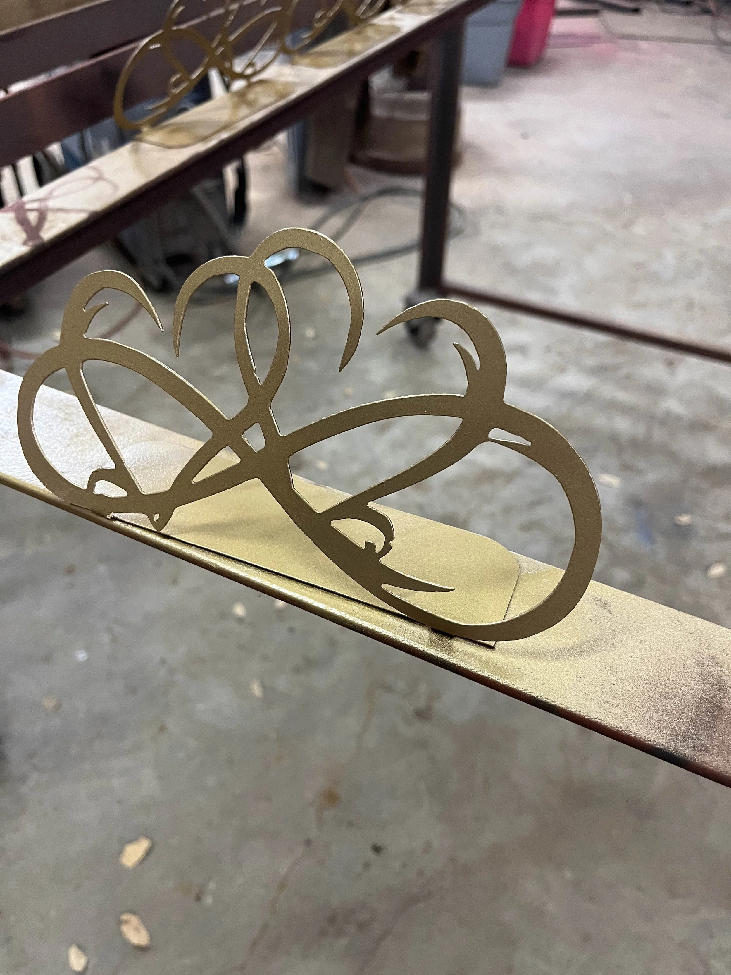 Close-up of a golden decorative metal piece with butterfly cutouts resting on a beige surface, with a metal table and store items in the background.