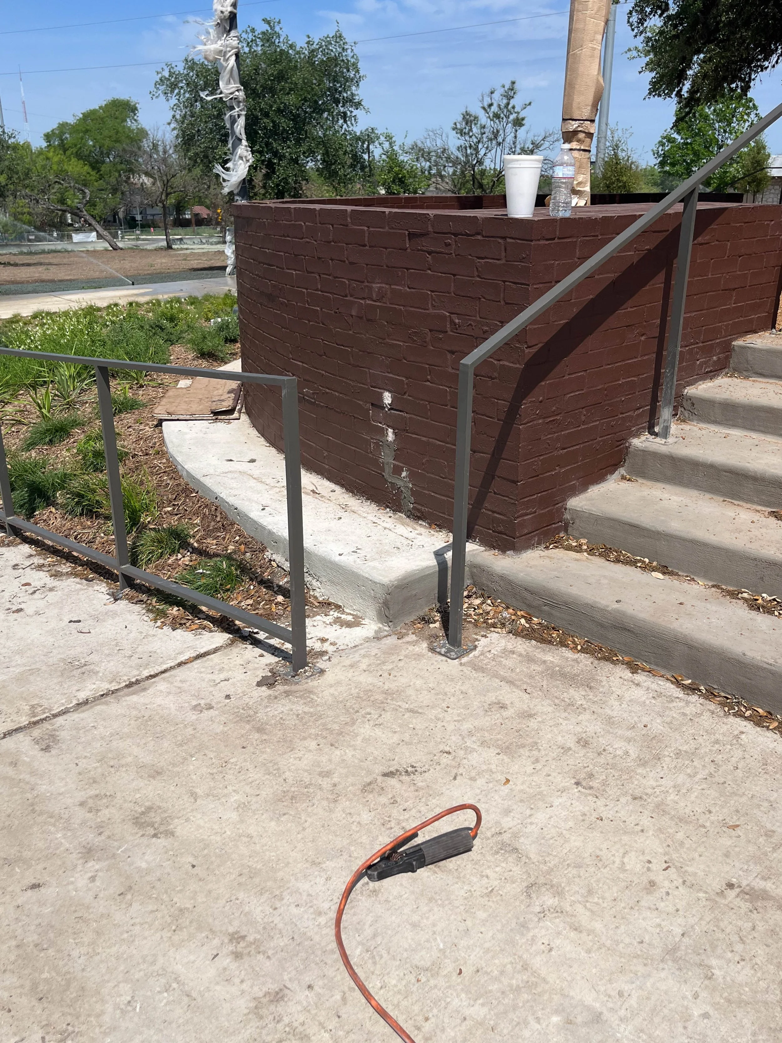 A brick structure with steps and a railing, a white styrofoam cup, a water bottle, and an electrical tool on the ground.
