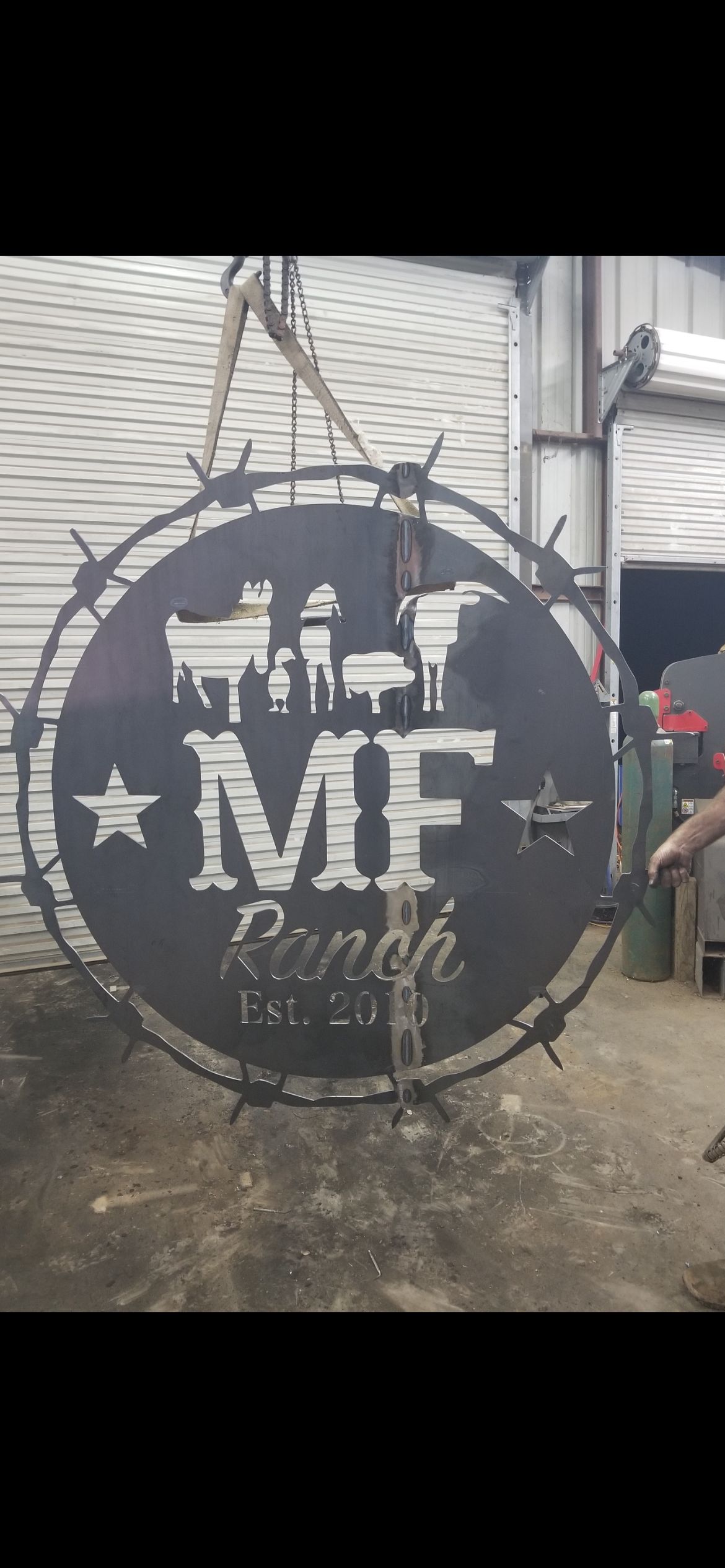 Metal sign with the text 'Mie Ranch Est. 2010' and decorative stars, surrounded by a barbed wire design, hanging in a workshop.