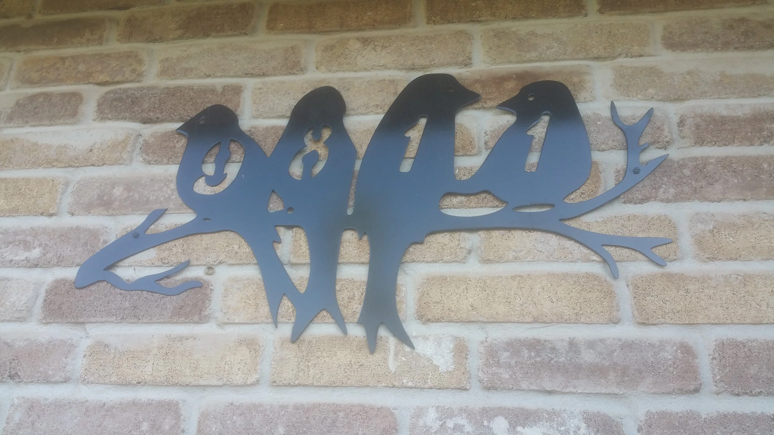 Metal wall art of a dinosaur, mounted on a brick wall.