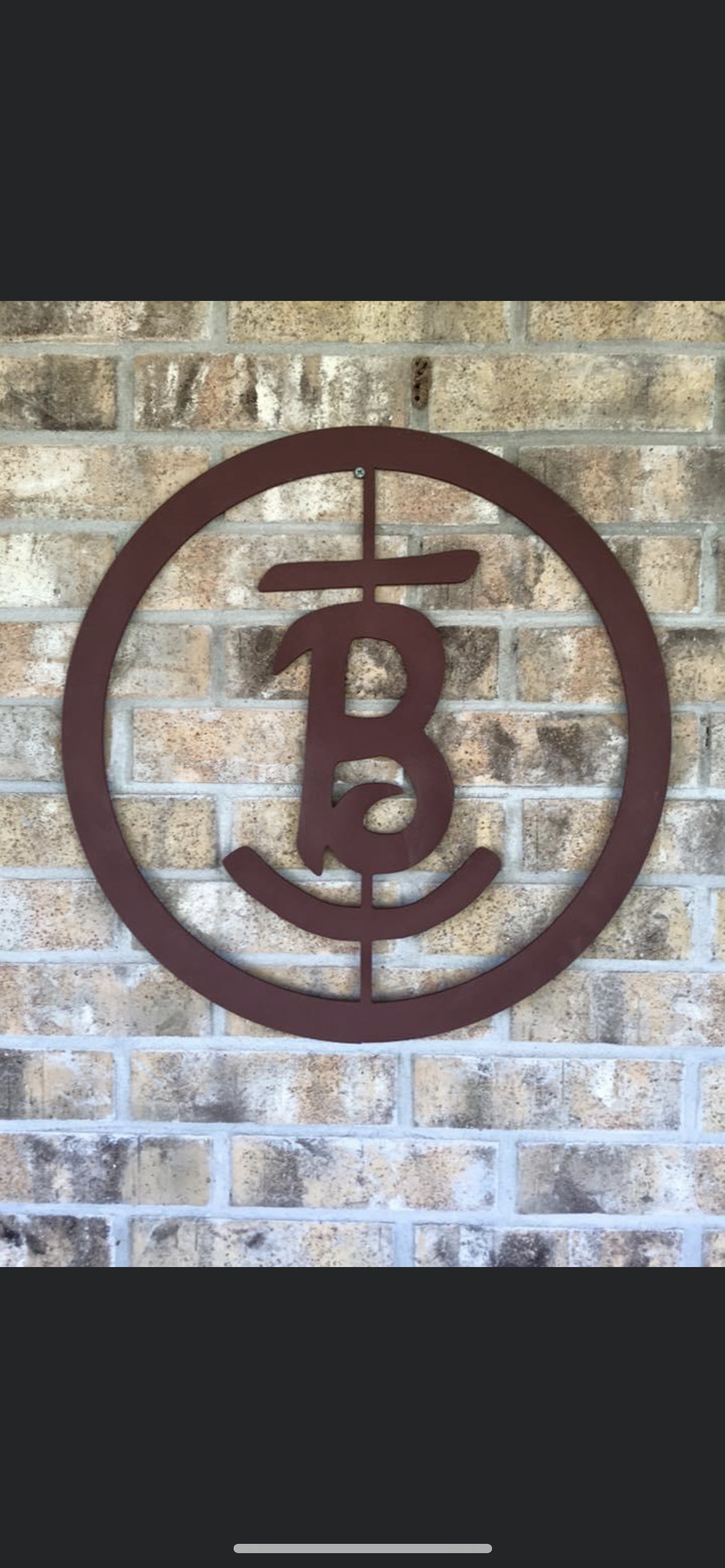 A round metal sign with a bicycle symbol and the letter 'B' in the center, mounted on a brick wall.