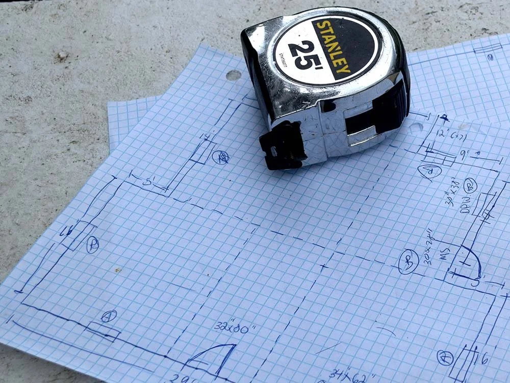 Blueprint or construction plan on graph paper with a tape measure on top.