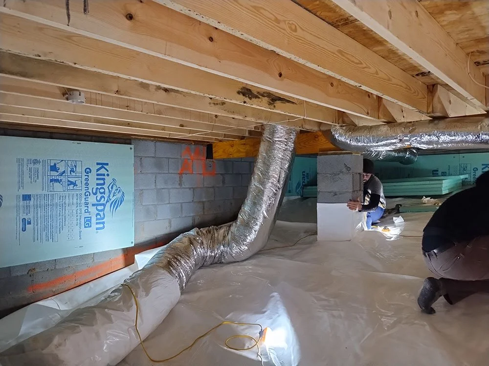 Construction workers installing ductwork and insulation in a basement,