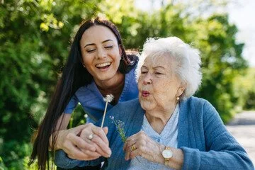 Young woman and elderly woman blowing bubbles outdoors in a green park.