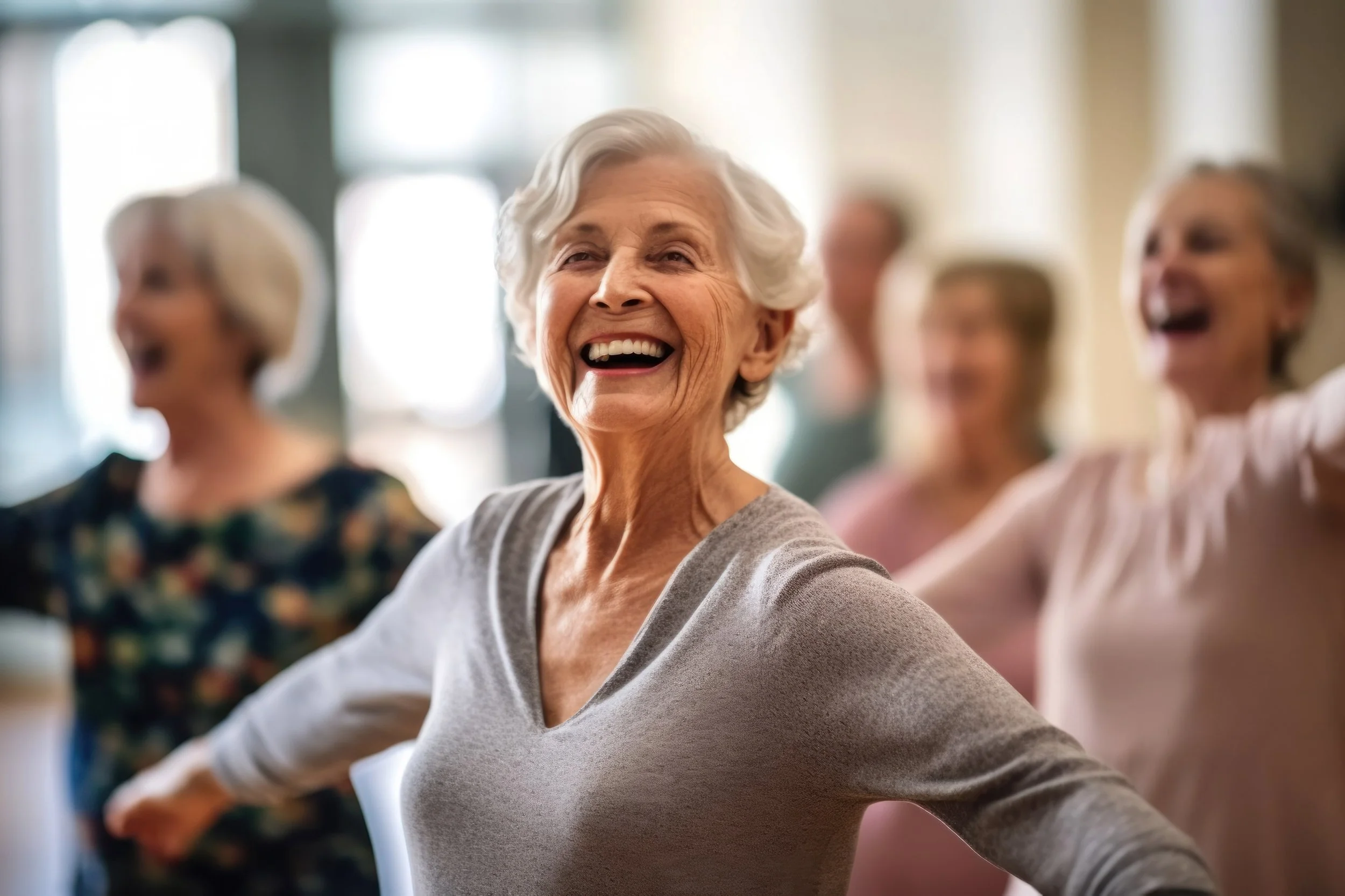 Group of elderly women sitting together, smiling, and laughing in a brightly lit room.