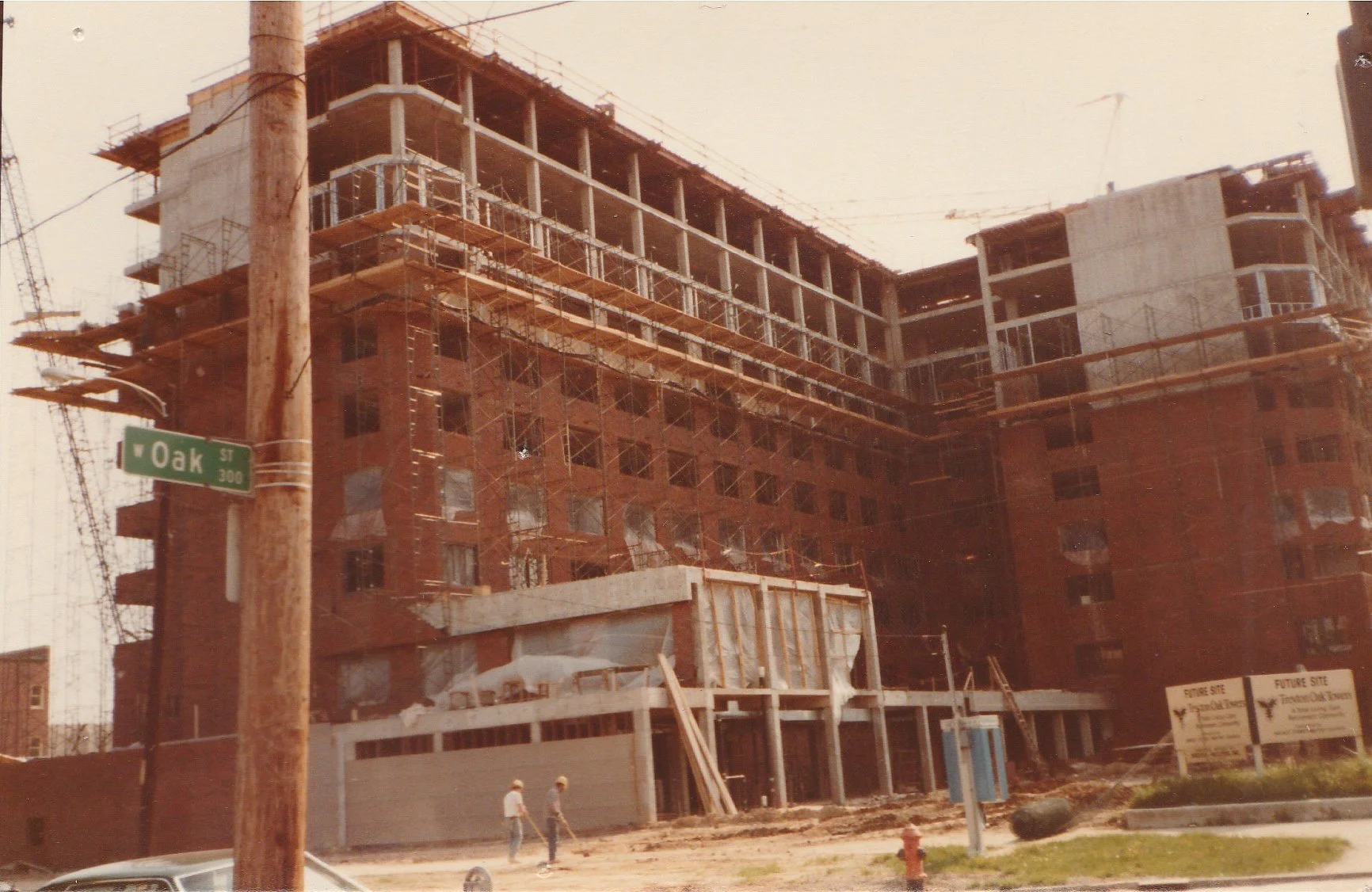 Construction site of a multi-story building with scaffolding, cranes, and workers, located at Oak Street.