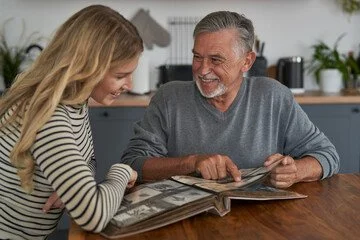 An older man and young girl sitting at a table looking through photo albums, smiling and sharing a moment together.