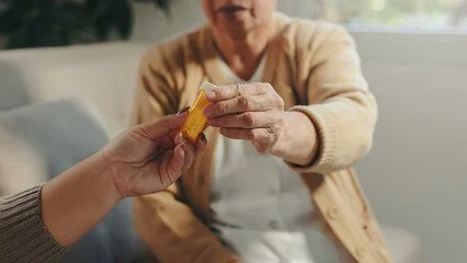 Close-up of a hand passing a yellow object, possibly a piece of food, to an elderly person in a beige sweater.