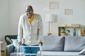 Elderly man using a walker in living room with sofa, tables, and artwork