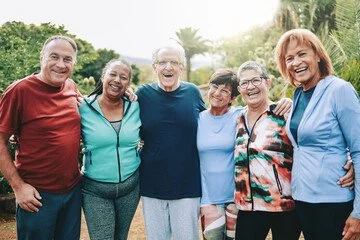 Group of six seniors smiling outdoors in a park or garden.