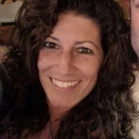 Close-up of a woman with dark, curly hair smiling at the camera