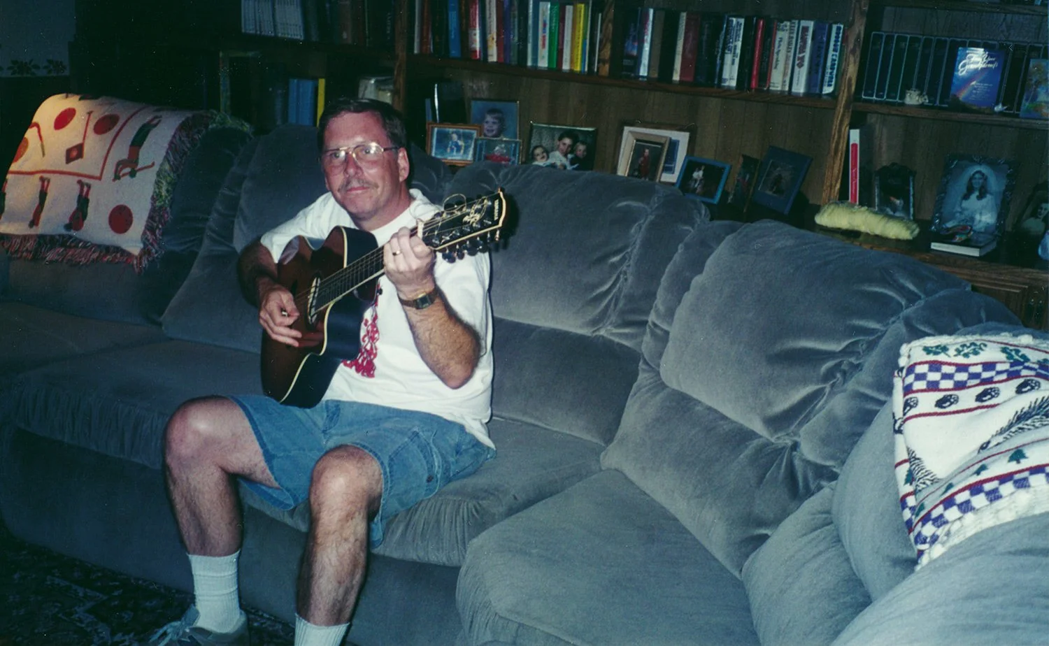 Brad Hartman sitting on a couch playing acoustic guitar at home in a candid family photograph.