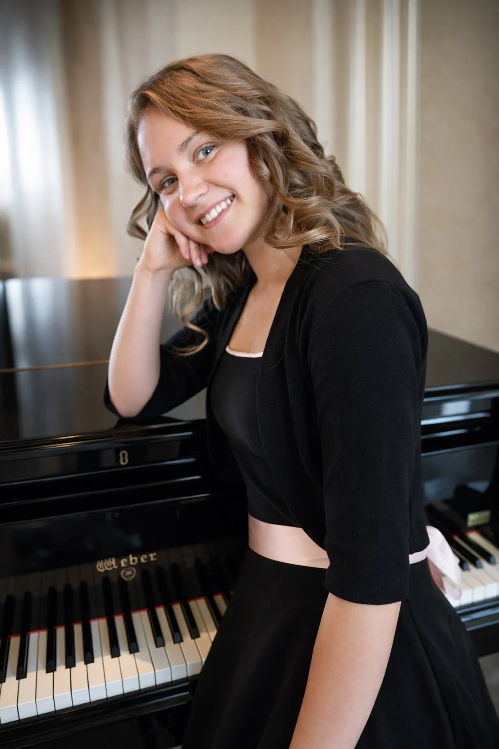 Piano instructor Chelsea Westbrook posing beside a grand piano at Hickory Arts in Hickory, NC.