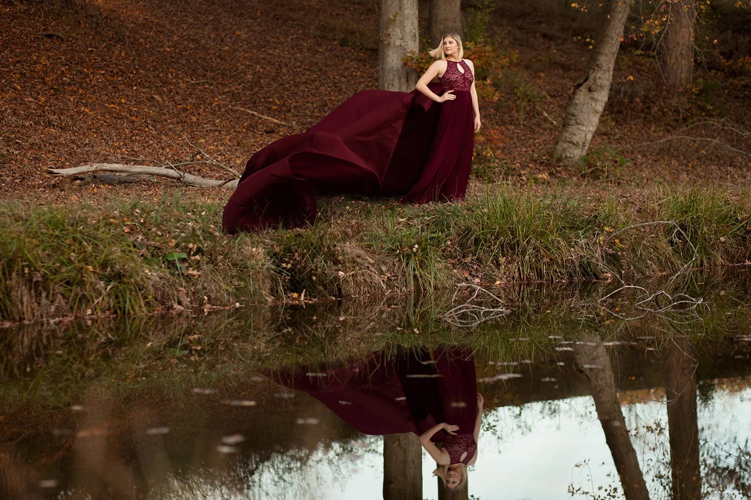 Young artist posing in a flowing formal dress beside a reflective creek during an artist development and creative portrait session connected to Hickory Arts in Hickory, NC.