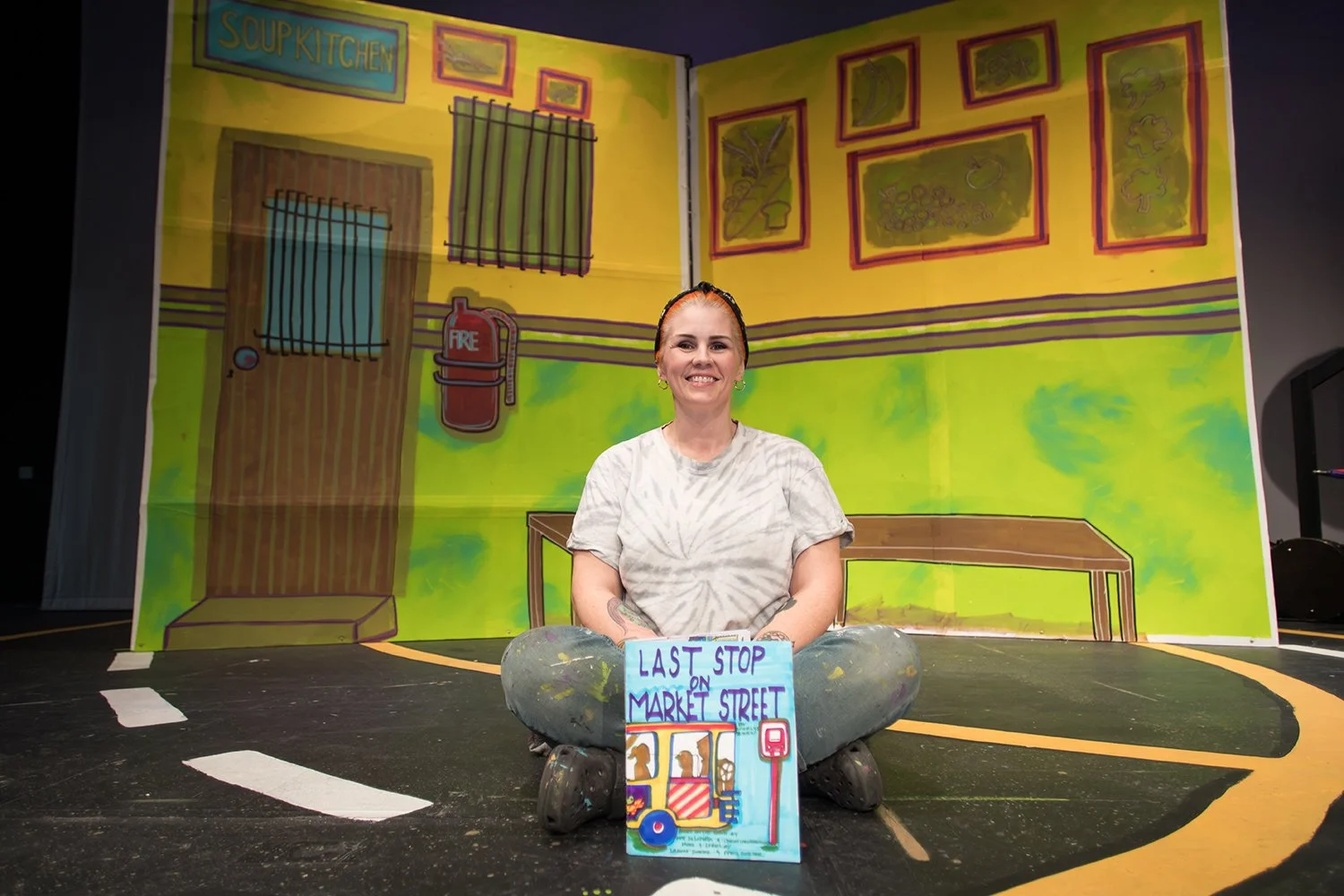 Rachael Morris sitting onstage in front of a colorful theatre set during a Hickory Arts production and audition prep experience in Hickory, NC.