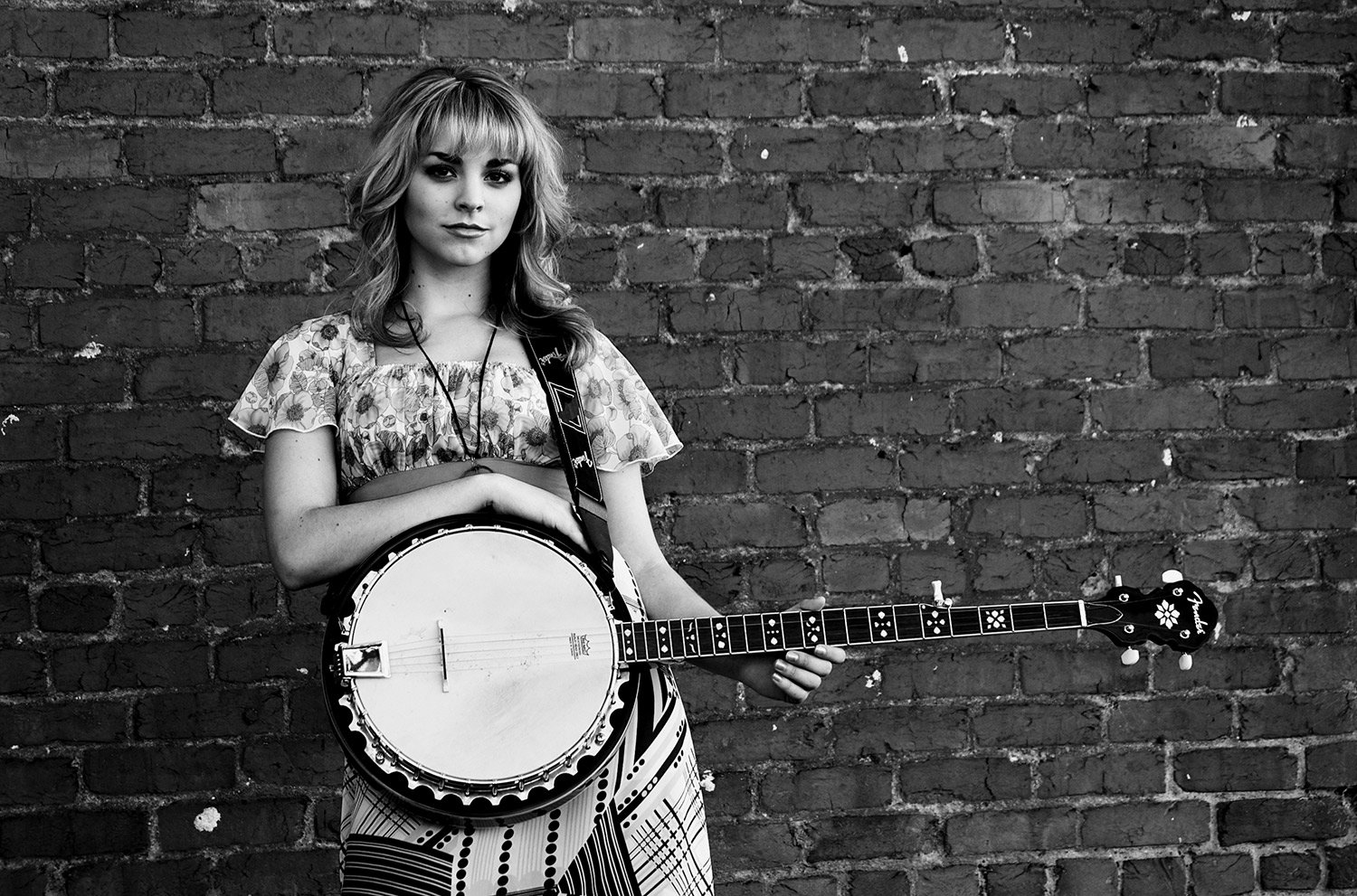 Black-and-white portrait of recording artist Sydney Torin Shepherd holding a banjo against a brick wall during a creative music session at Hickory Arts in North Carolina.