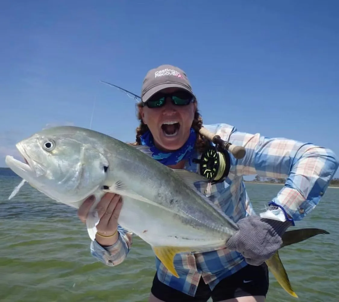 Person holding a large fish on a boat with water and blue sky in the background.