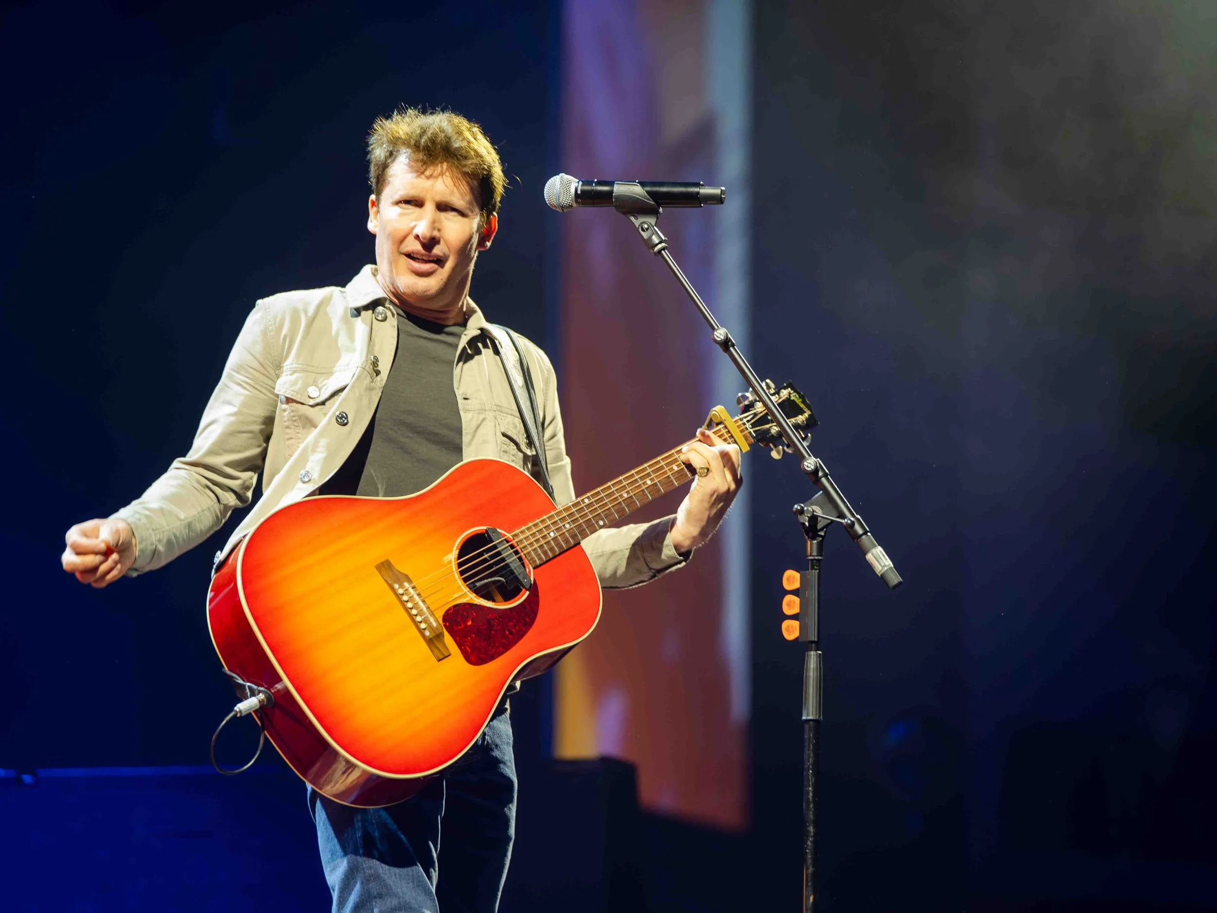 James Blunt performing, holding a guitar, and facing the camera at the Utilita arena in Cardiff.
