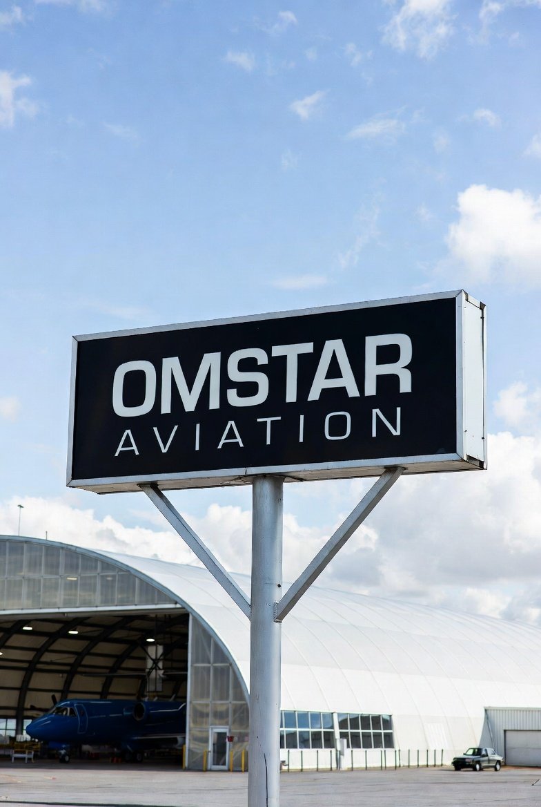 Sign for Omstar Aviation near an airport hangar with an aircraft inside.