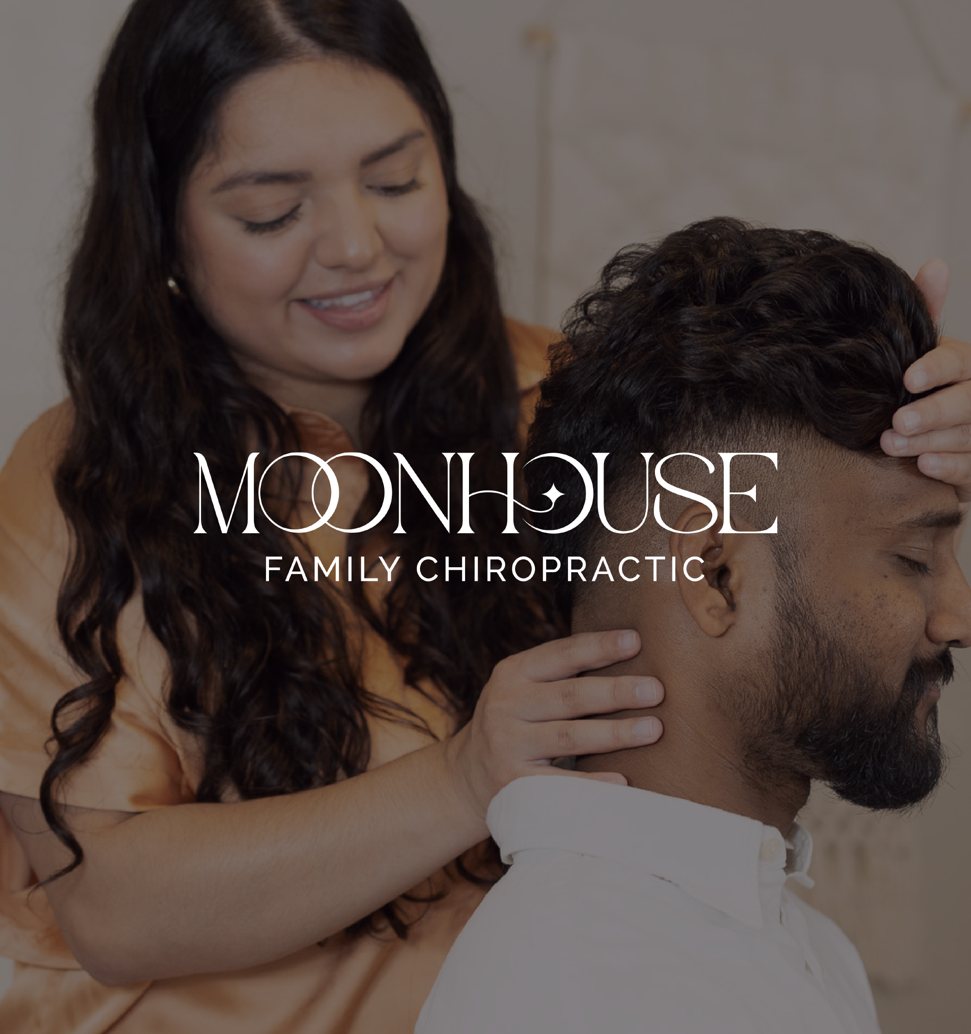 A woman with long dark hair gently holds a man's head, who has short dark curly hair, in what appears to be a chiropractic or massage setting.