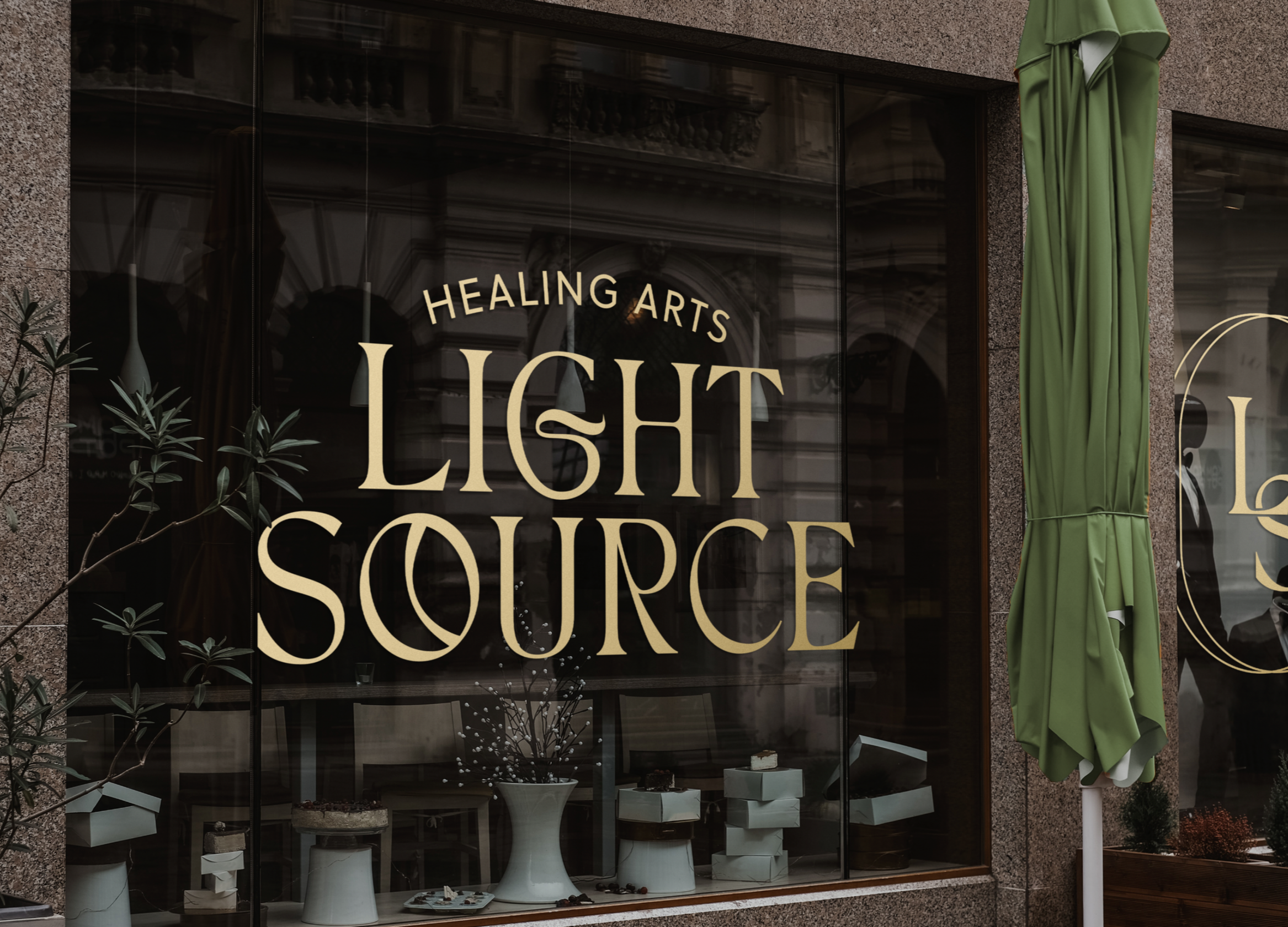 storefront window with sign reading 'Healing Arts Light Source,' with green curtain on the right and plants visible through the glass. Holisitic Branding