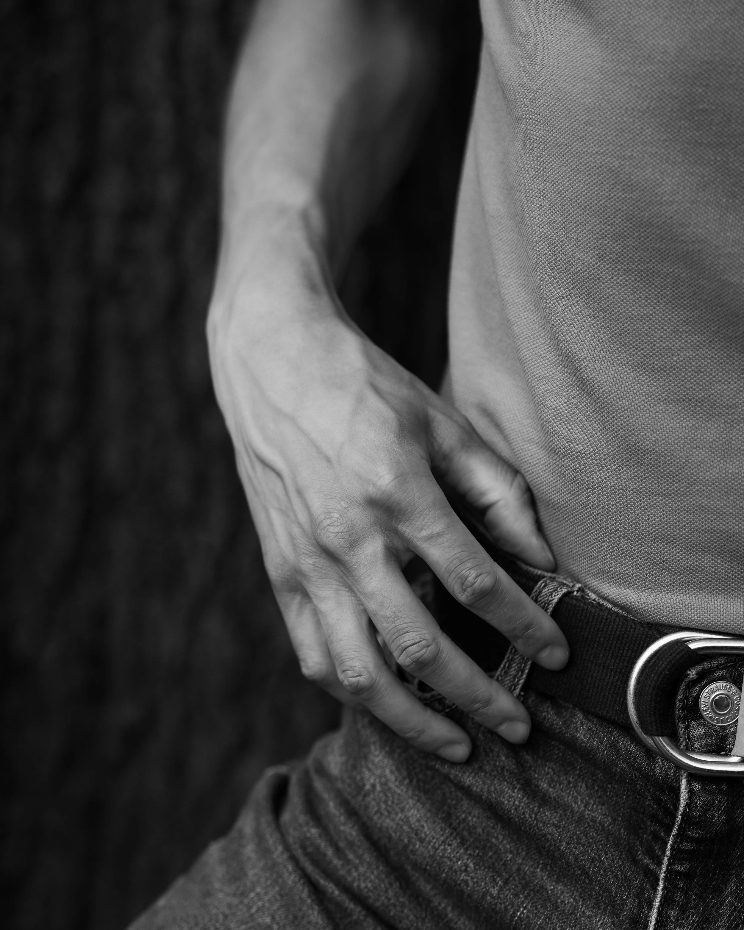 Close-up of a person's hand and fingers resting on their lap, wearing a ring with the Levi's logo on it, in black and white.