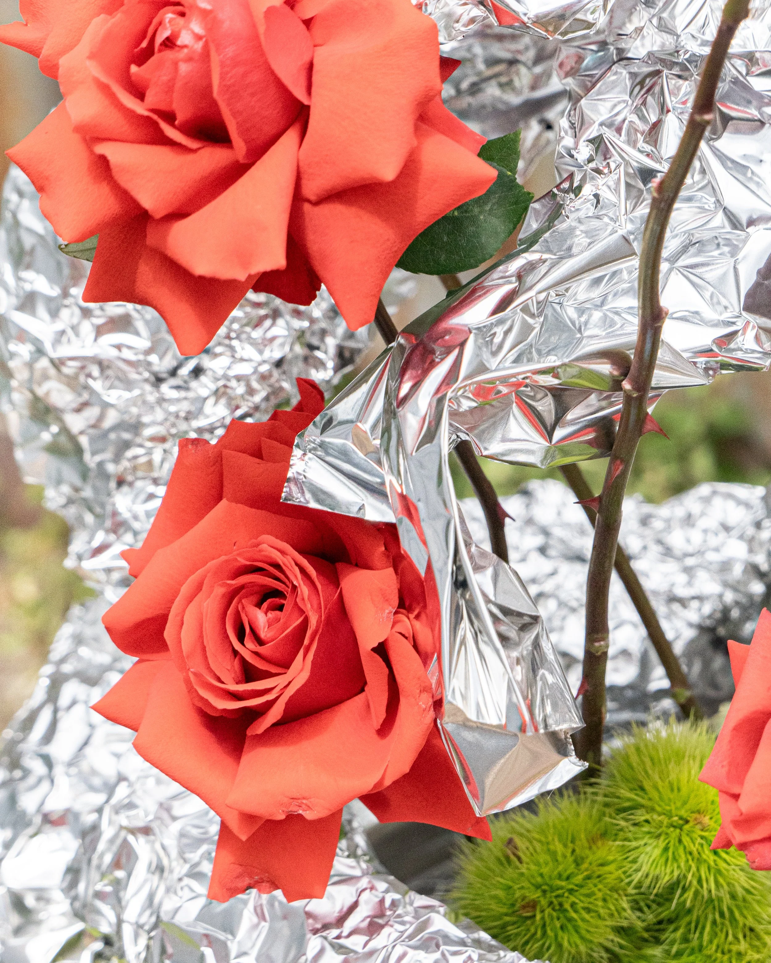 Close-up of a red artificial rose surrounded by crumpled aluminum foil and some green fern leaves.